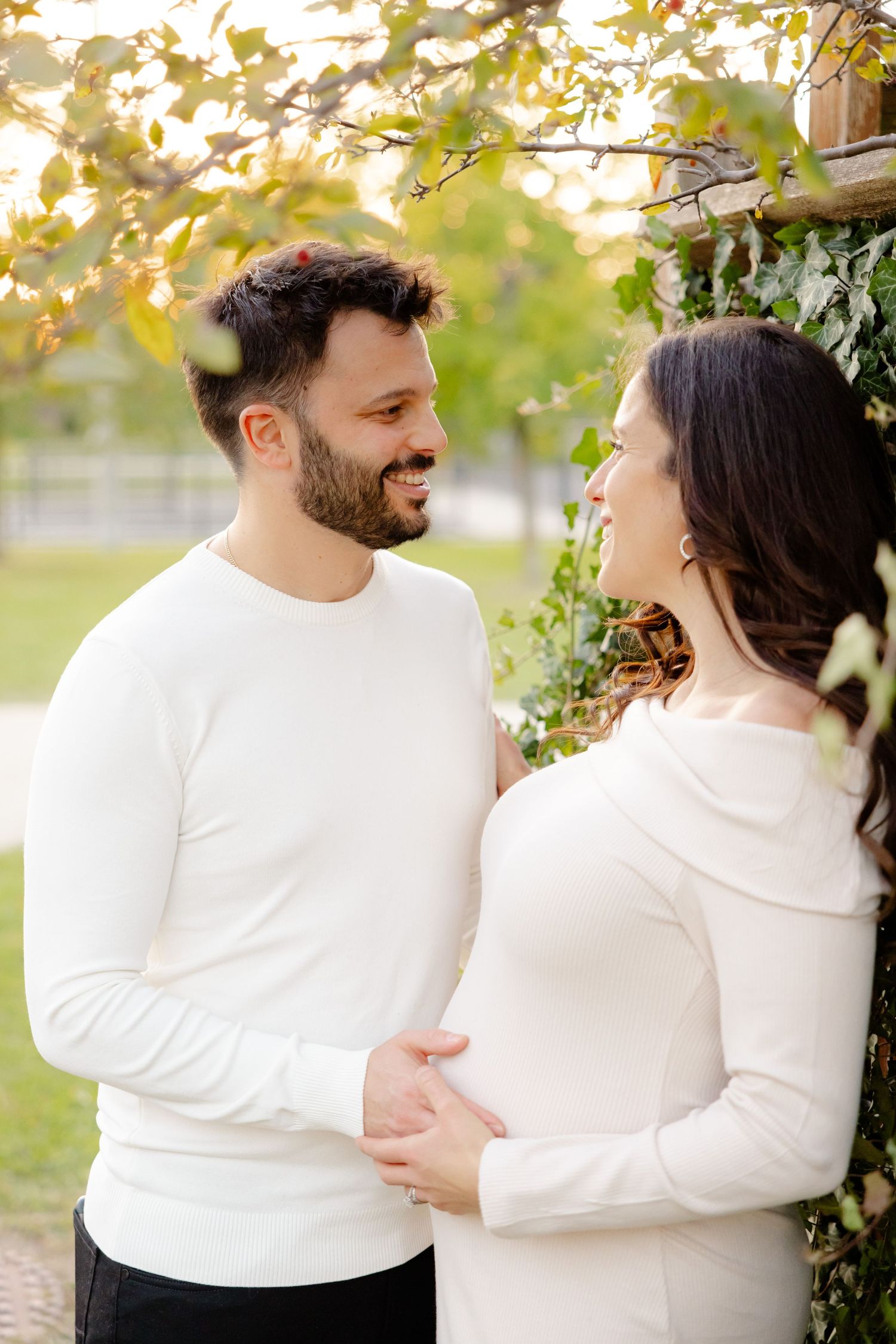 Couple in white tops embrace outdoors among autumn foliage, sharing an intimate moment.