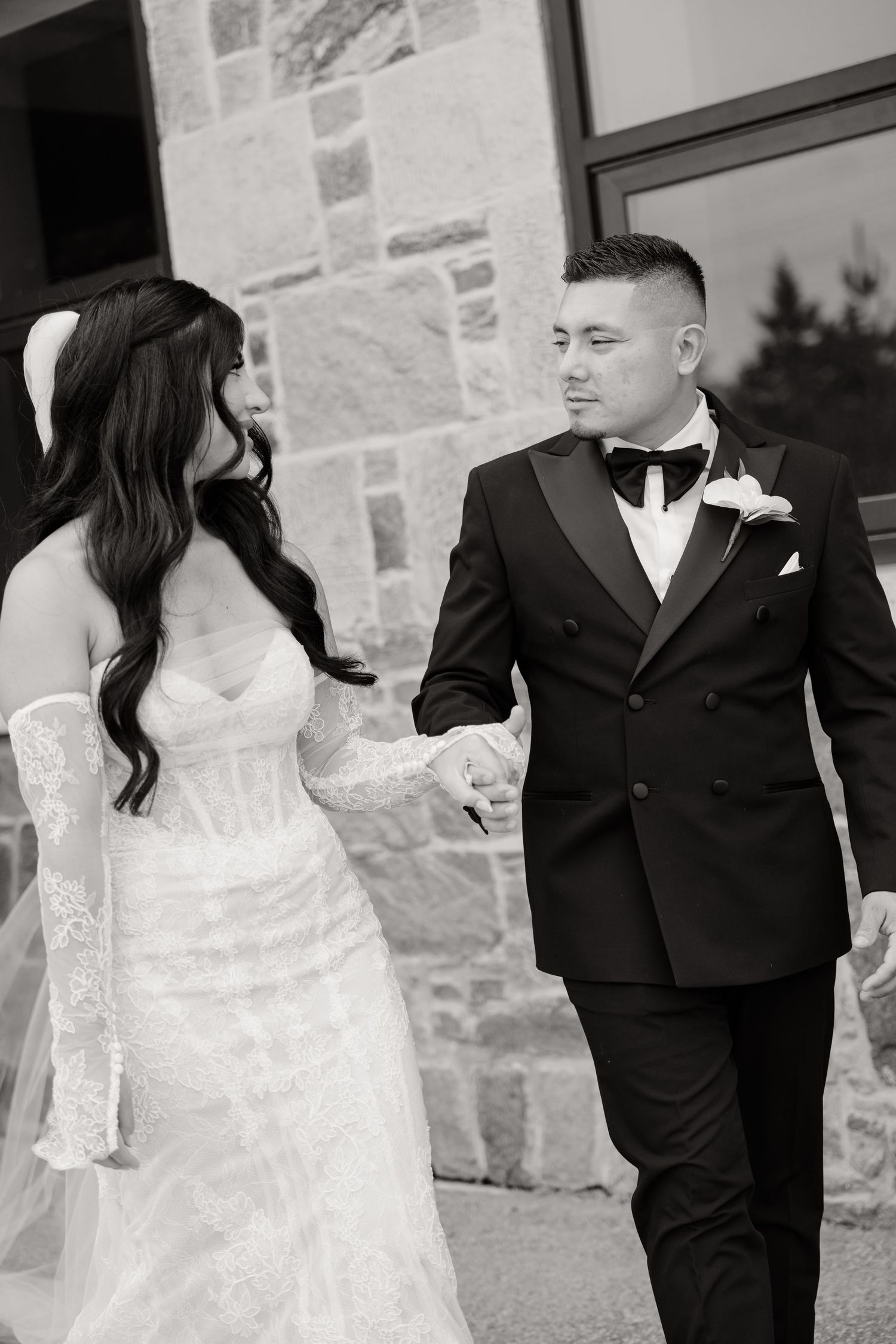 A bride and groom share an affectionate moment while taking outdoor wedding photos against a stone wall background.