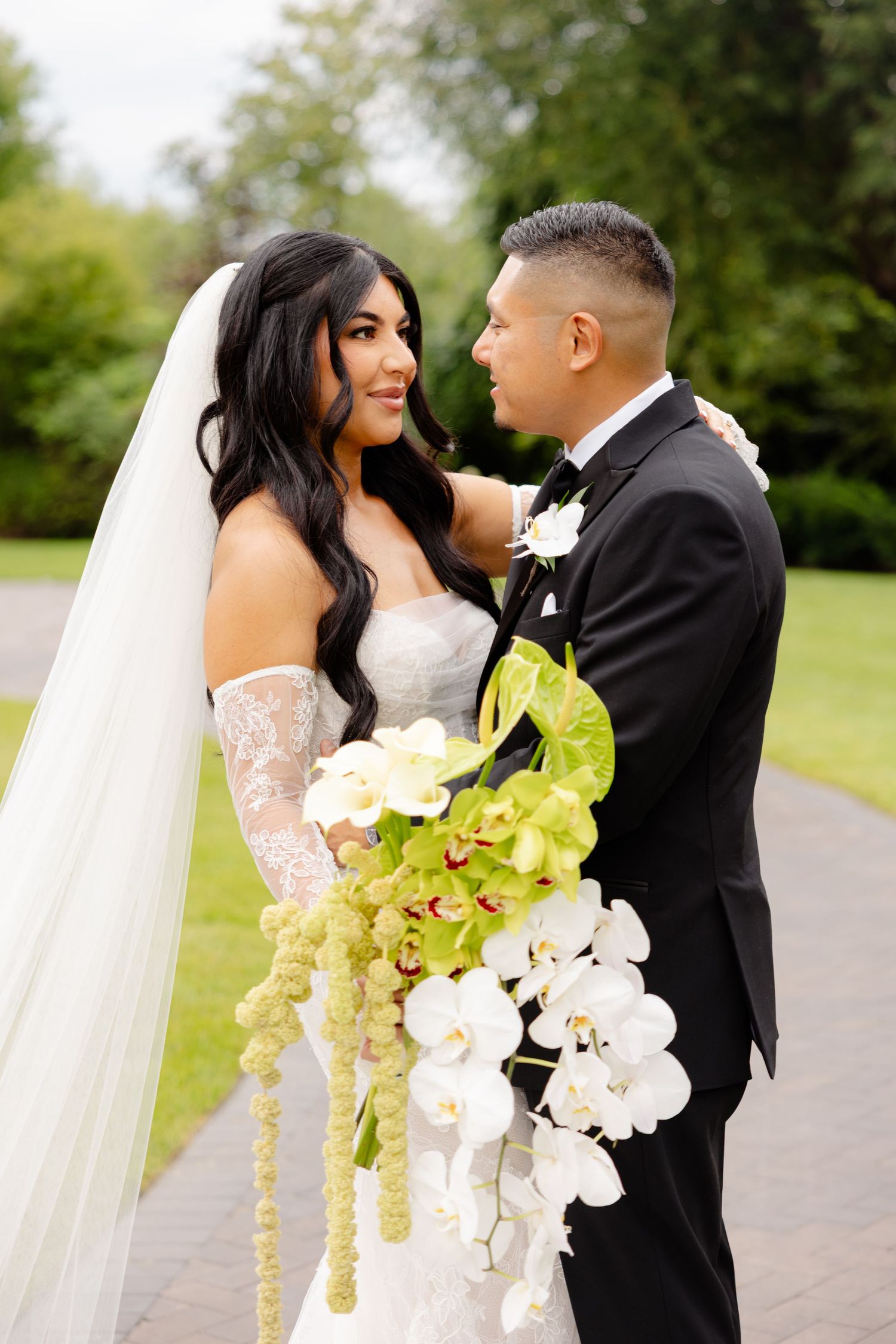 A bride and groom share an intimate moment outdoors with cascading white orchids and greenery in their wedding photos.