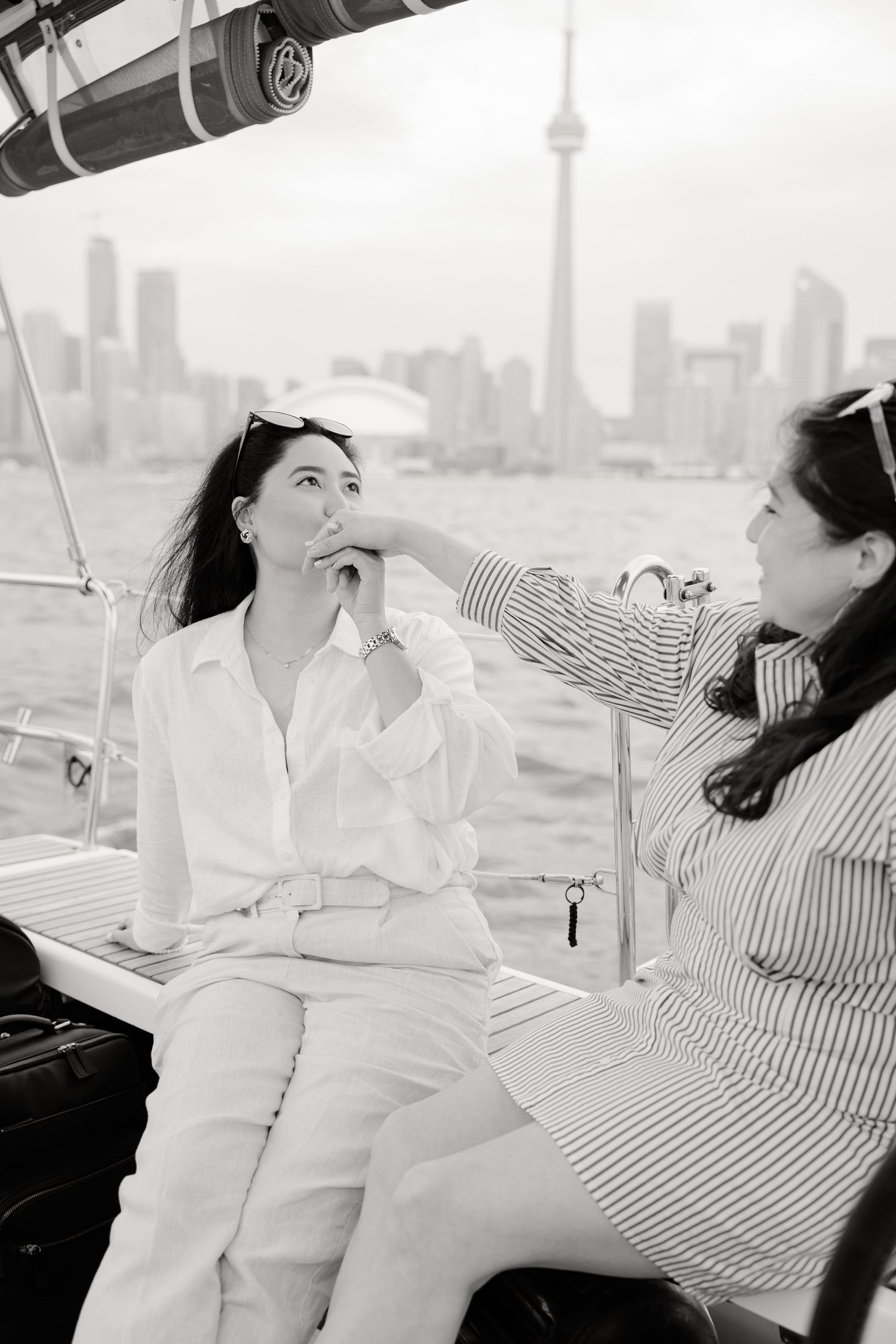 Two people relaxing on a boat with Toronto's CN Tower skyline visible in the misty background.