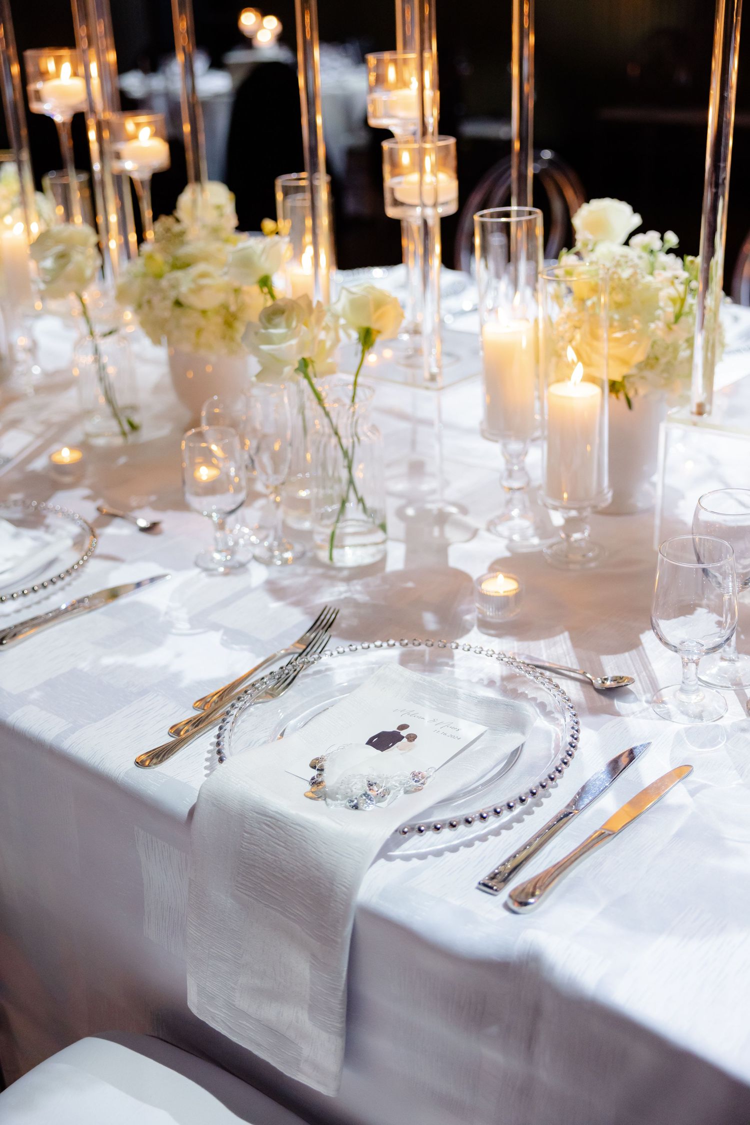 Elegant wedding table setting with white flowers, crystal chargers and glowing candles.