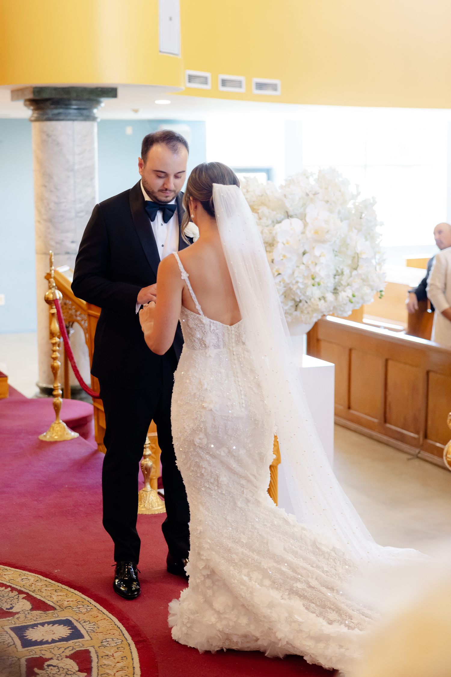 A couple in formal wedding attire sharing a special moment together in a church setting with white floral decorations.