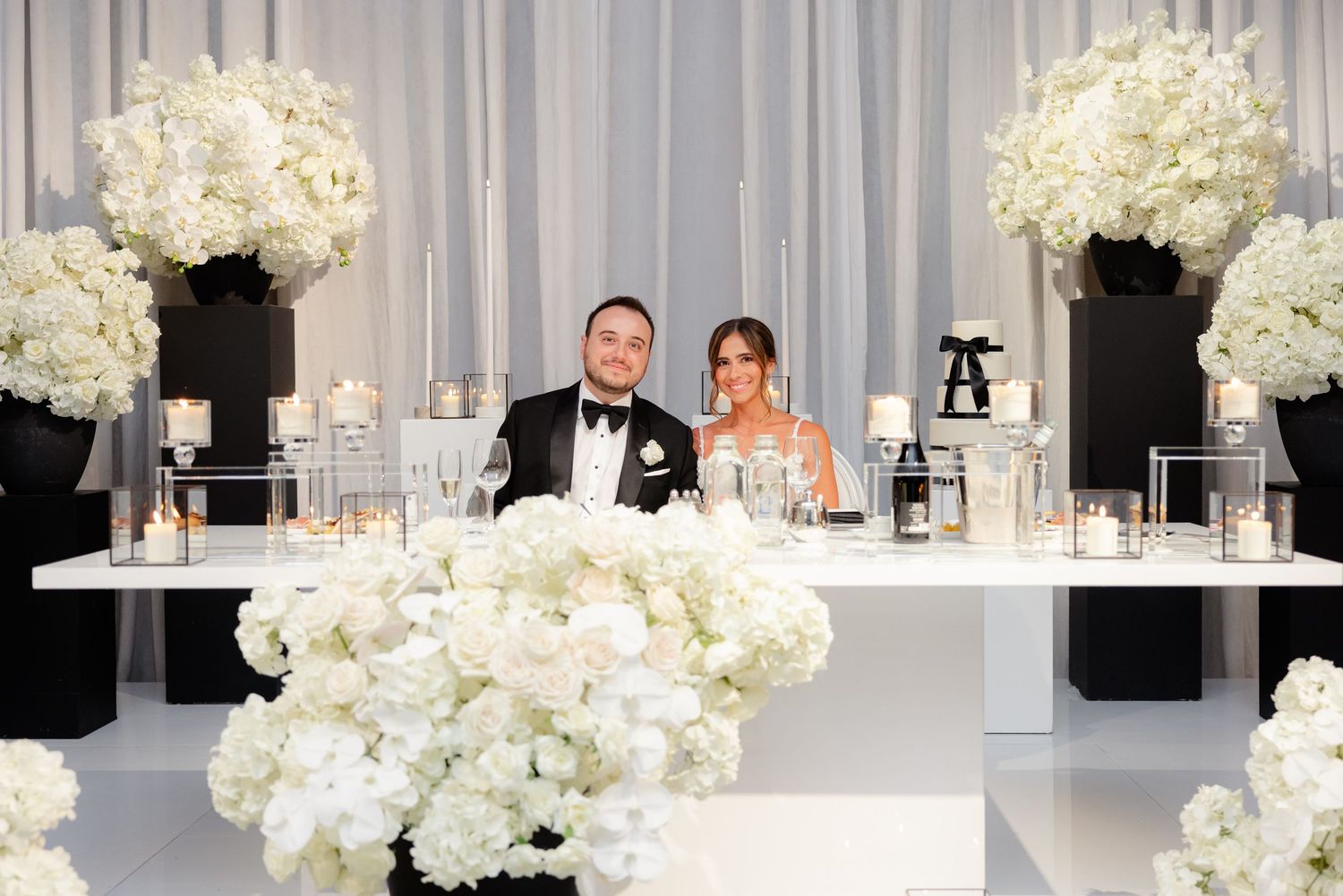 Elegant wedding reception setup with white hydrangea centerpieces and formal black and white decor at head table.