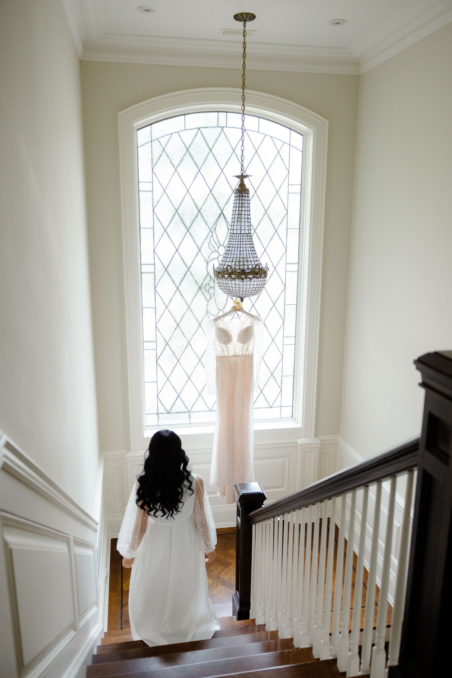 Romantic bridal scene with wedding dress and chandelier illuminated by arched window light.