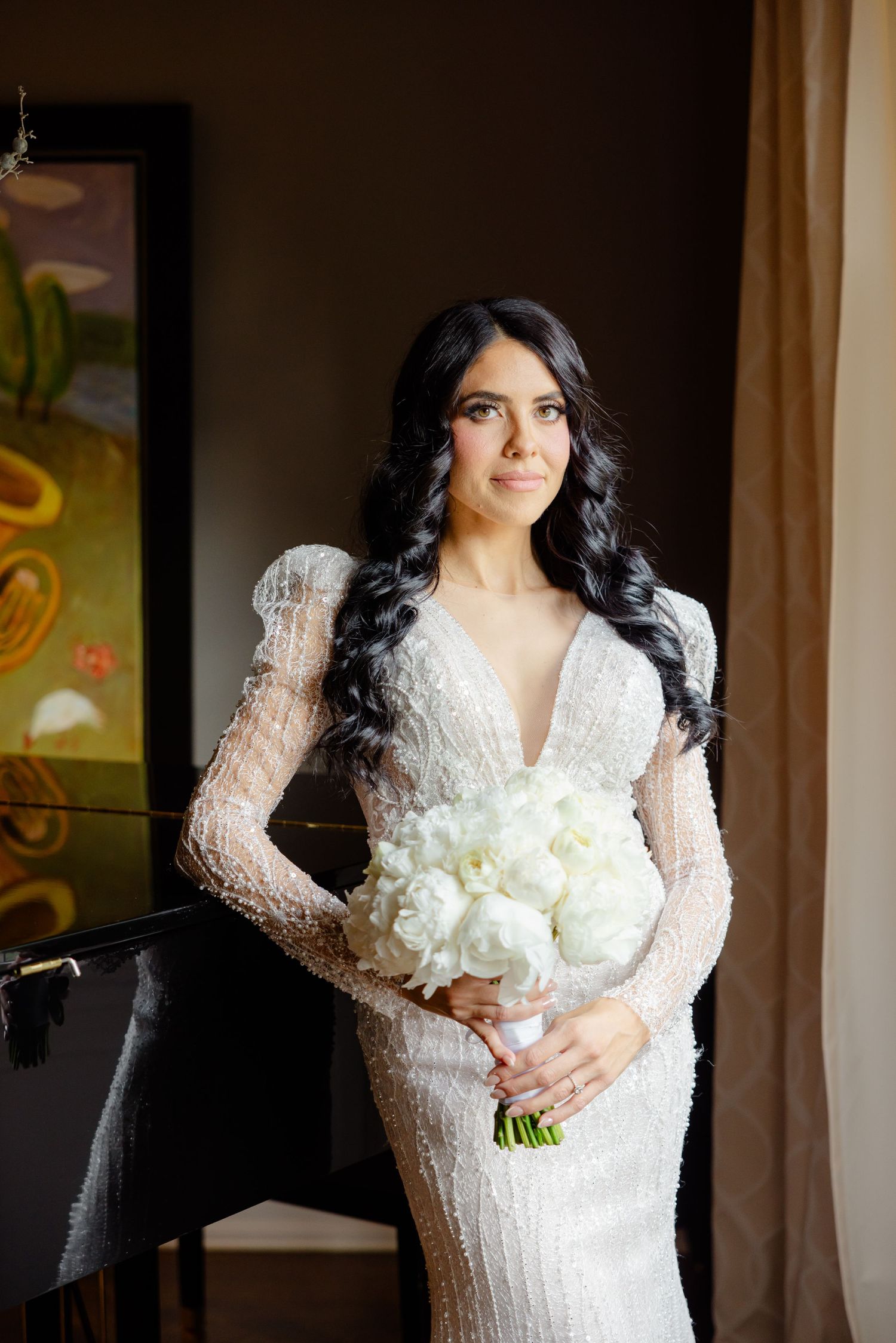 Elegant wedding dress with long lace sleeves and a white bouquet in an indoor setting with natural light.