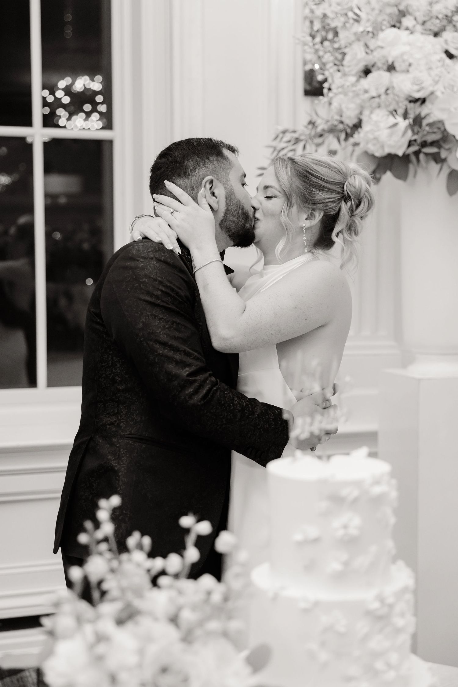 Black and white intimate moment between newlyweds beside their wedding cake.