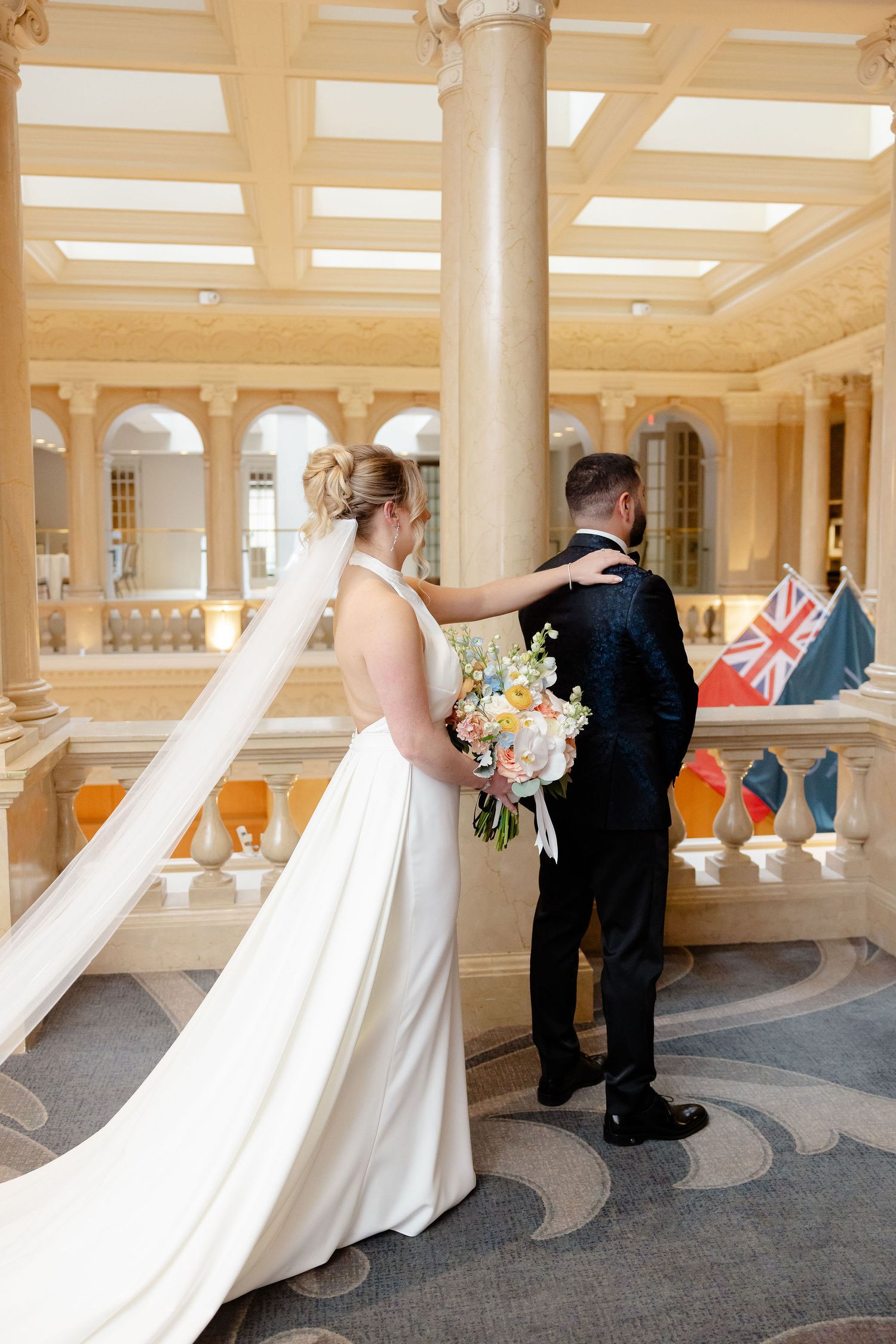 Wedding party poses in grand columned hallway with ornate architecture and flowing white dress.