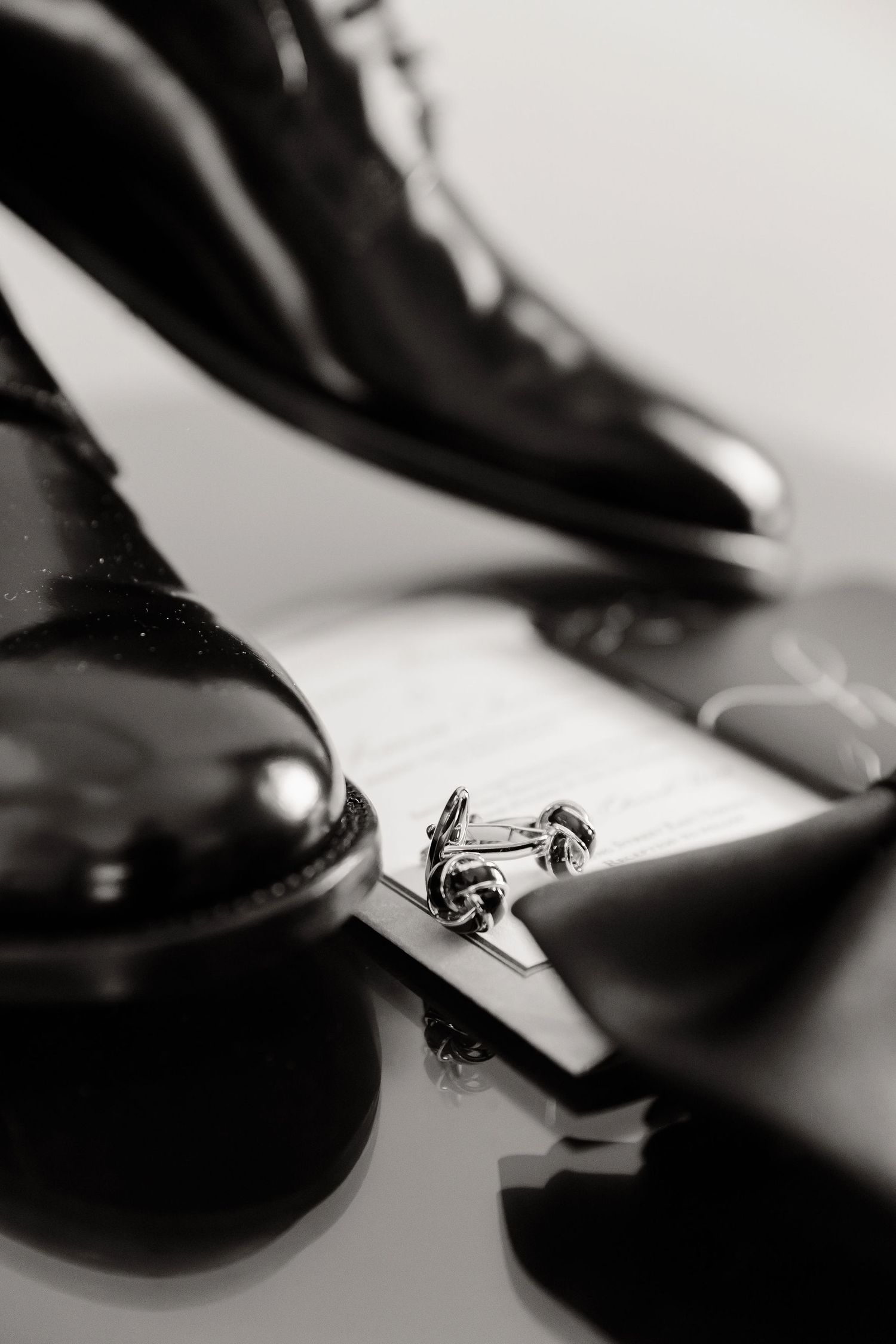 Black formal dress shoes with cufflinks placed on reflective surface in dramatic black and white photography.
