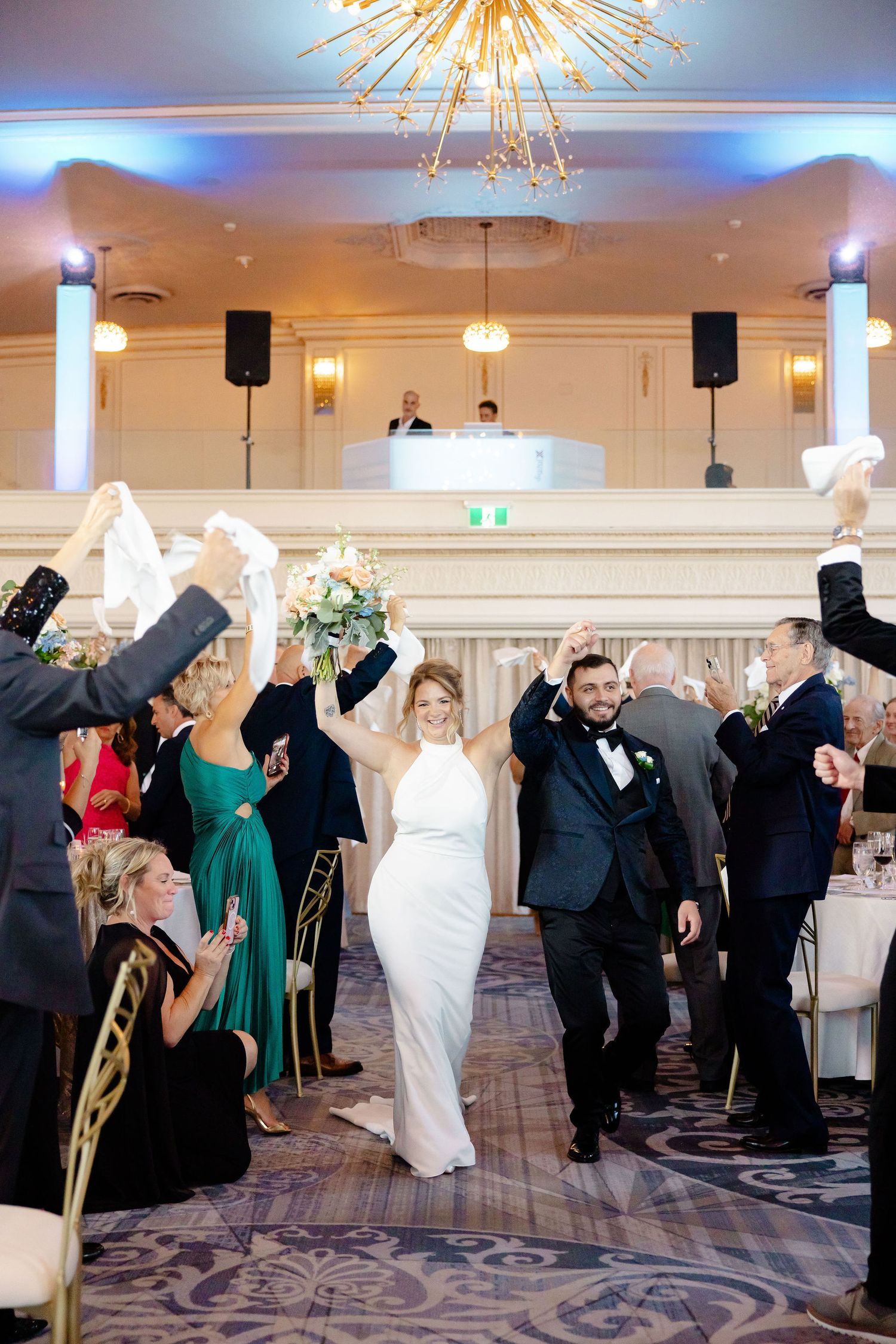 Wedding guests dance and celebrate on an elegant ballroom dance floor under crystal chandeliers.