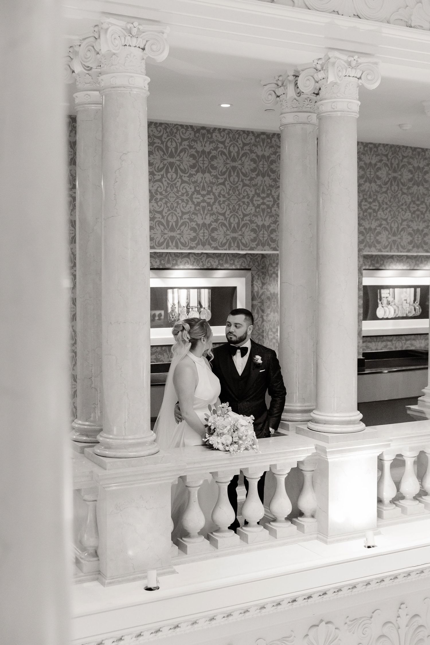 Elegant interior balcony with white columns and damask wallpaper showcases wedding couple.