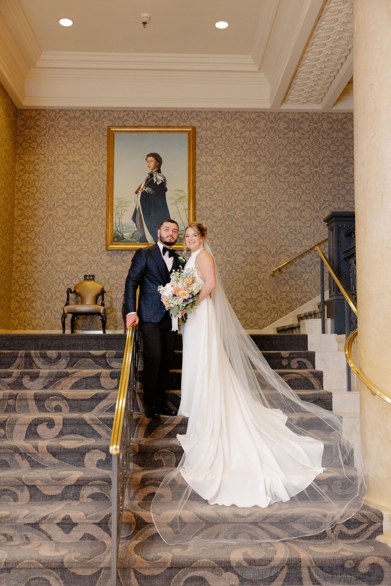 A wedding couple shares a romantic first look moment on an elegant staircase with gold railings.
