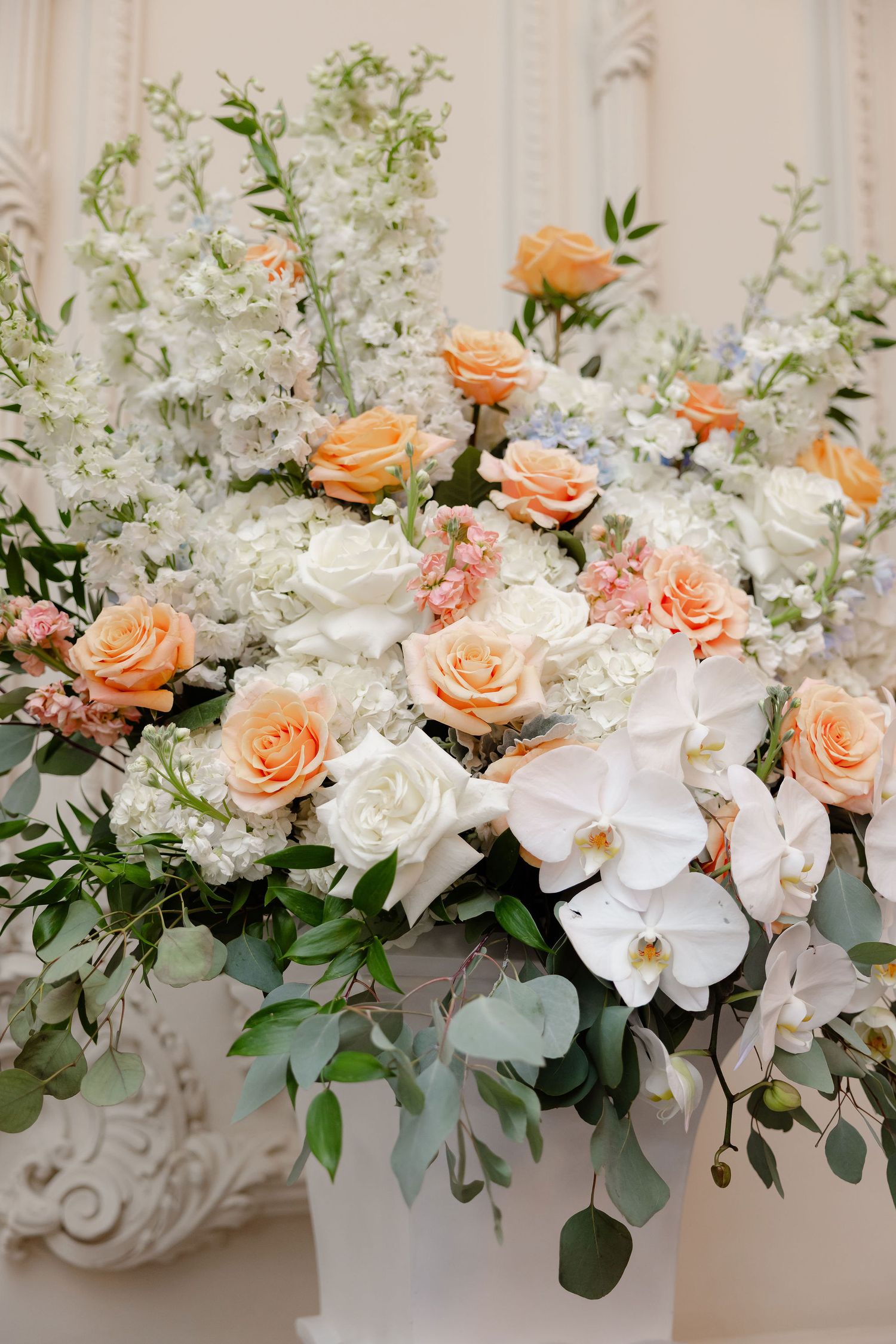 A luxurious floral arrangement combines peach roses, white orchids and delicate greenery for a wedding centerpiece.