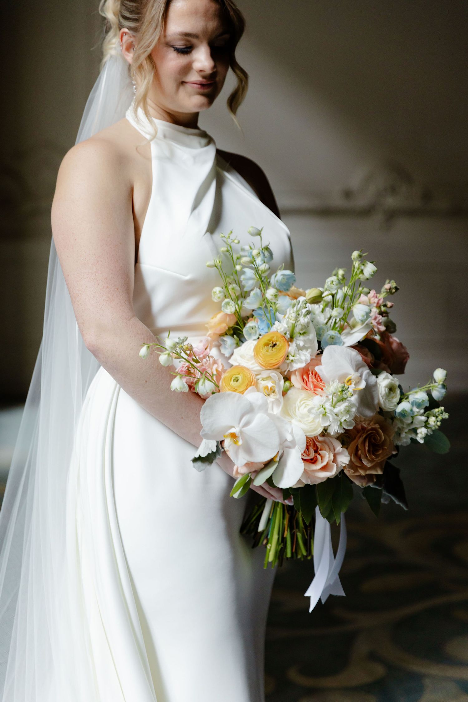Bride holds romantic peach and white floral bouquet in high-neck white wedding gown.