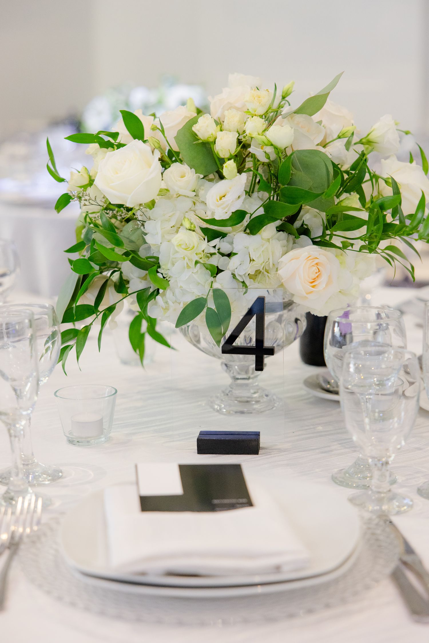 Elegant white floral centerpiece with roses and greenery next to table number 4 at wedding reception.