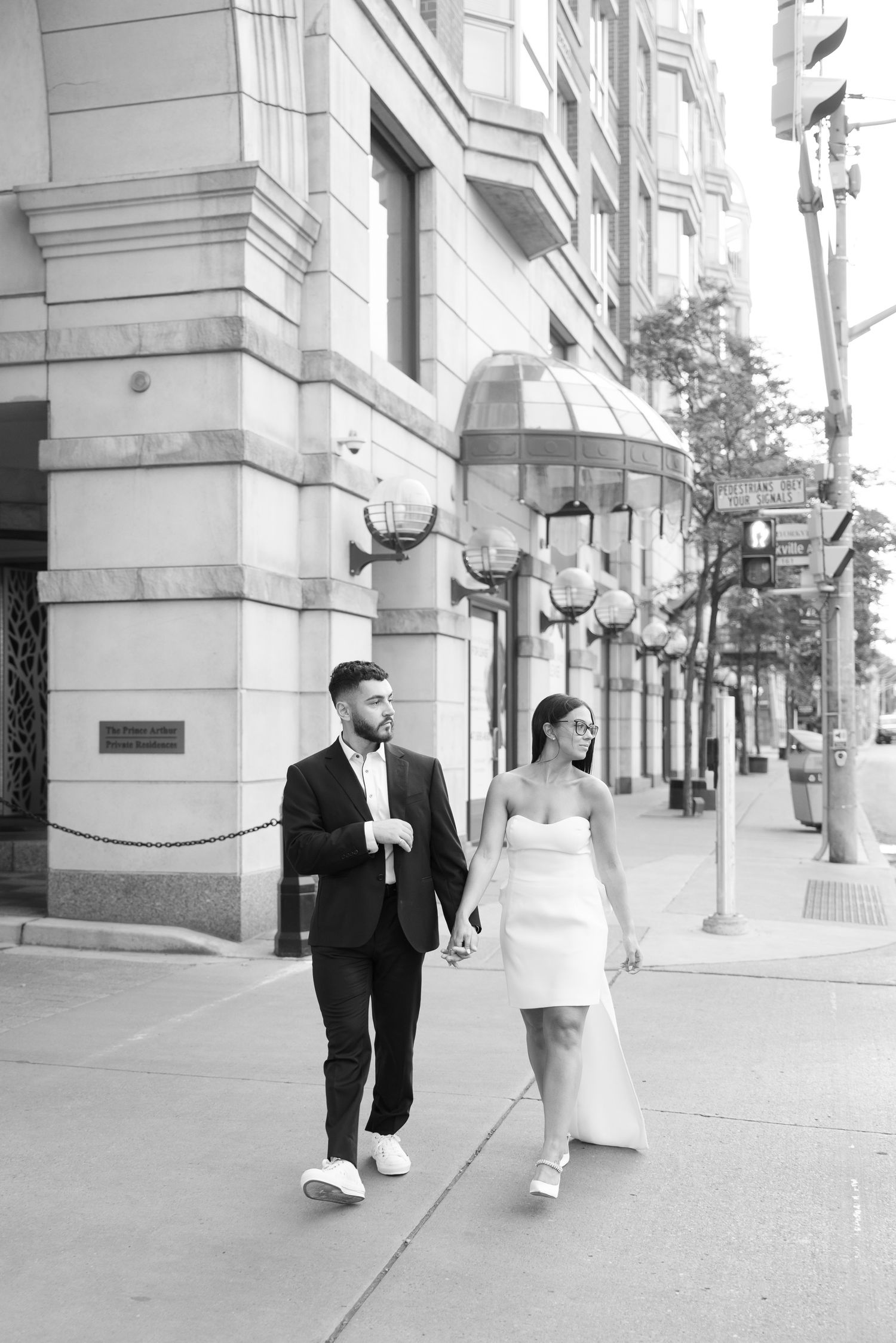 Couple strolling together along an urban sidewalk with classical architecture in the background.
