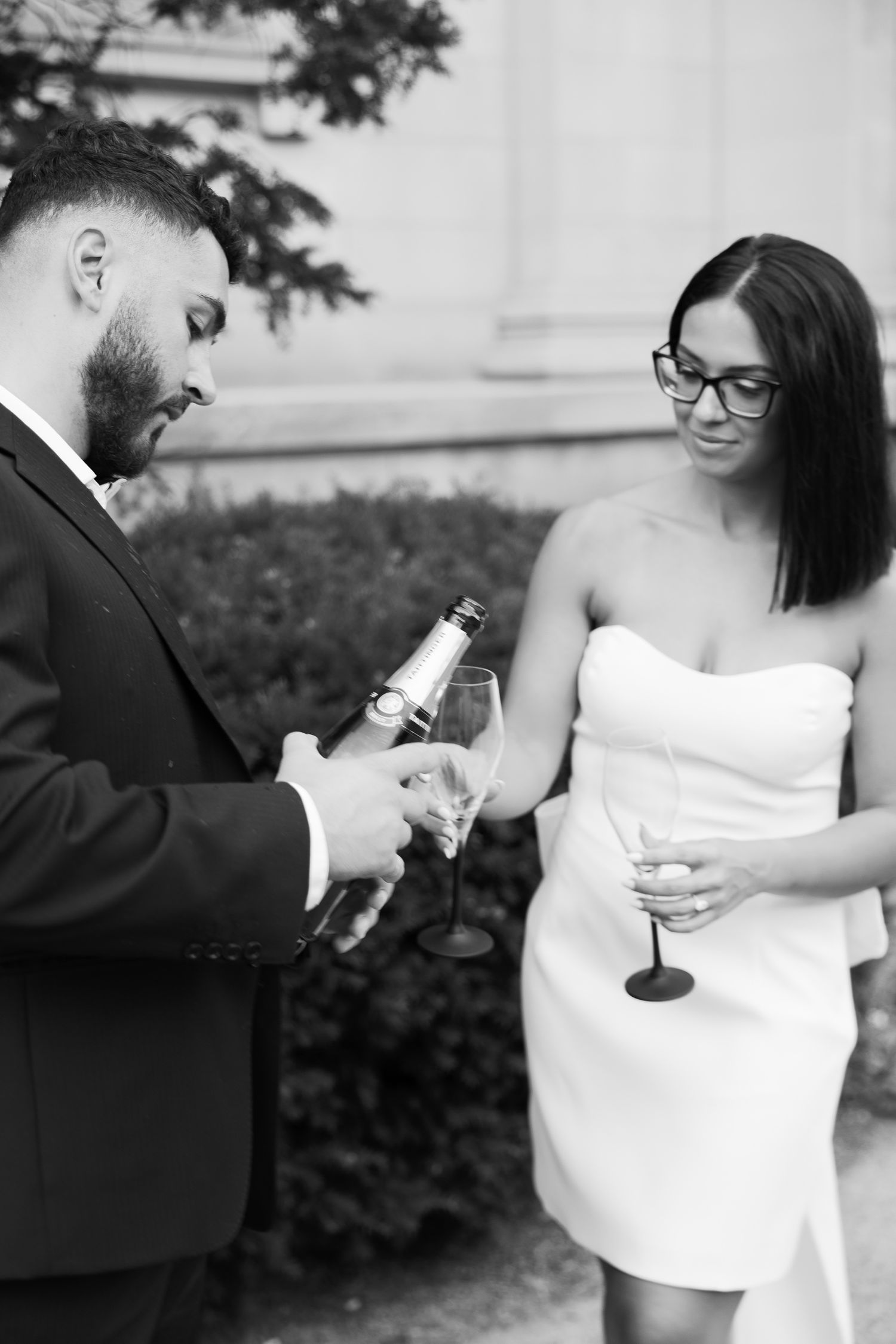 A black and white moment of a couple preparing to toast with champagne outdoors.