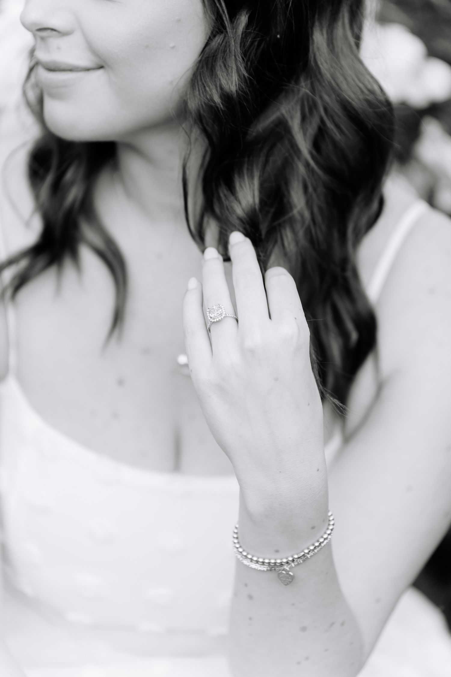 Close-up black and white shot of a hand wearing an engagement ring and bracelet.