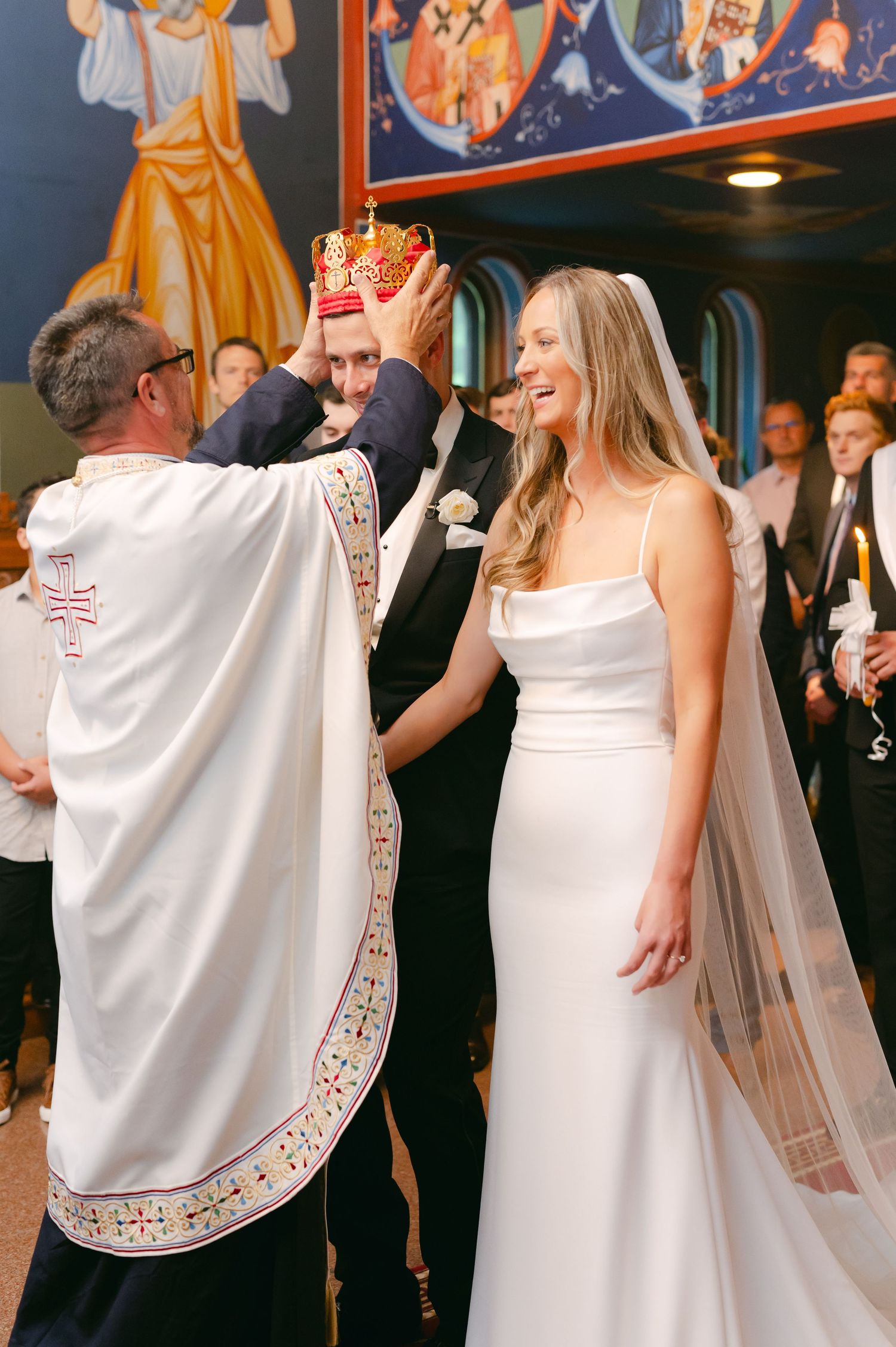 Wedding ceremony in an Orthodox church with priest placing crowns during traditional marriage rites.