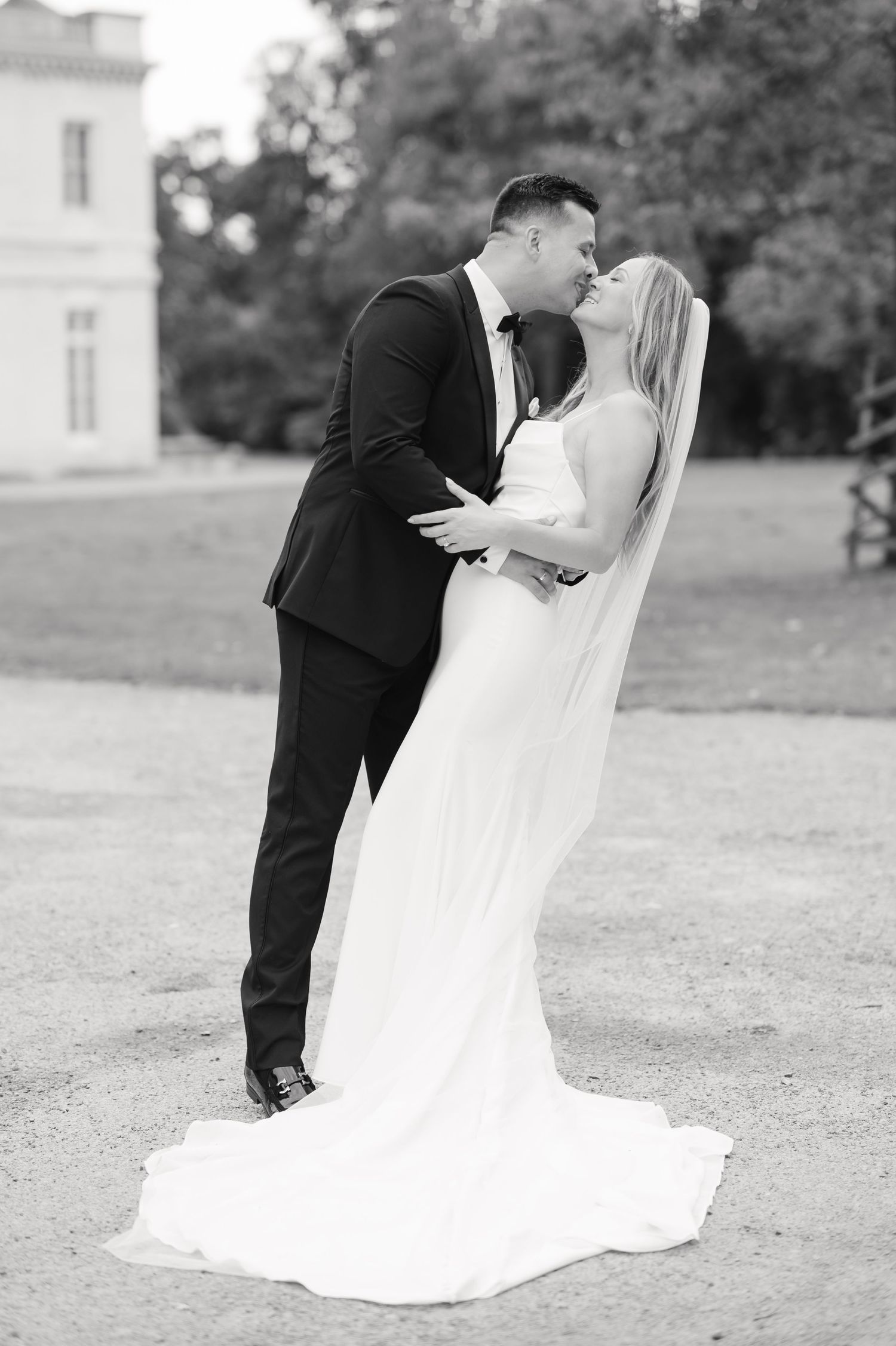 A black and white wedding portrait of a couple sharing a romantic kiss outdoors.