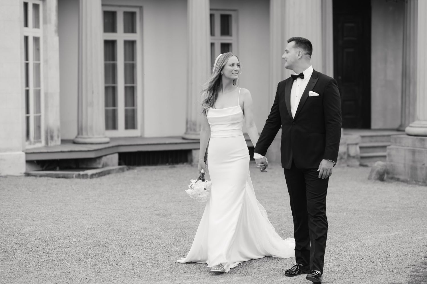 Black and white photo of couple walking together on estate grounds in wedding attire.