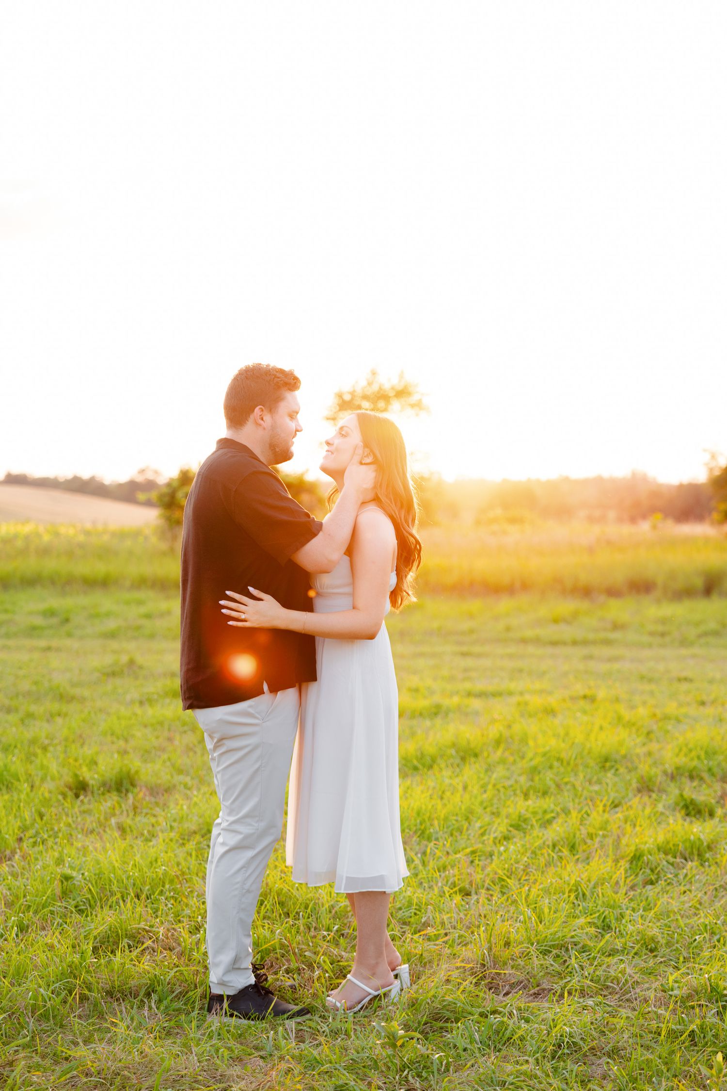 Couple embraces in golden sunset light during outdoor photoshoot in field.