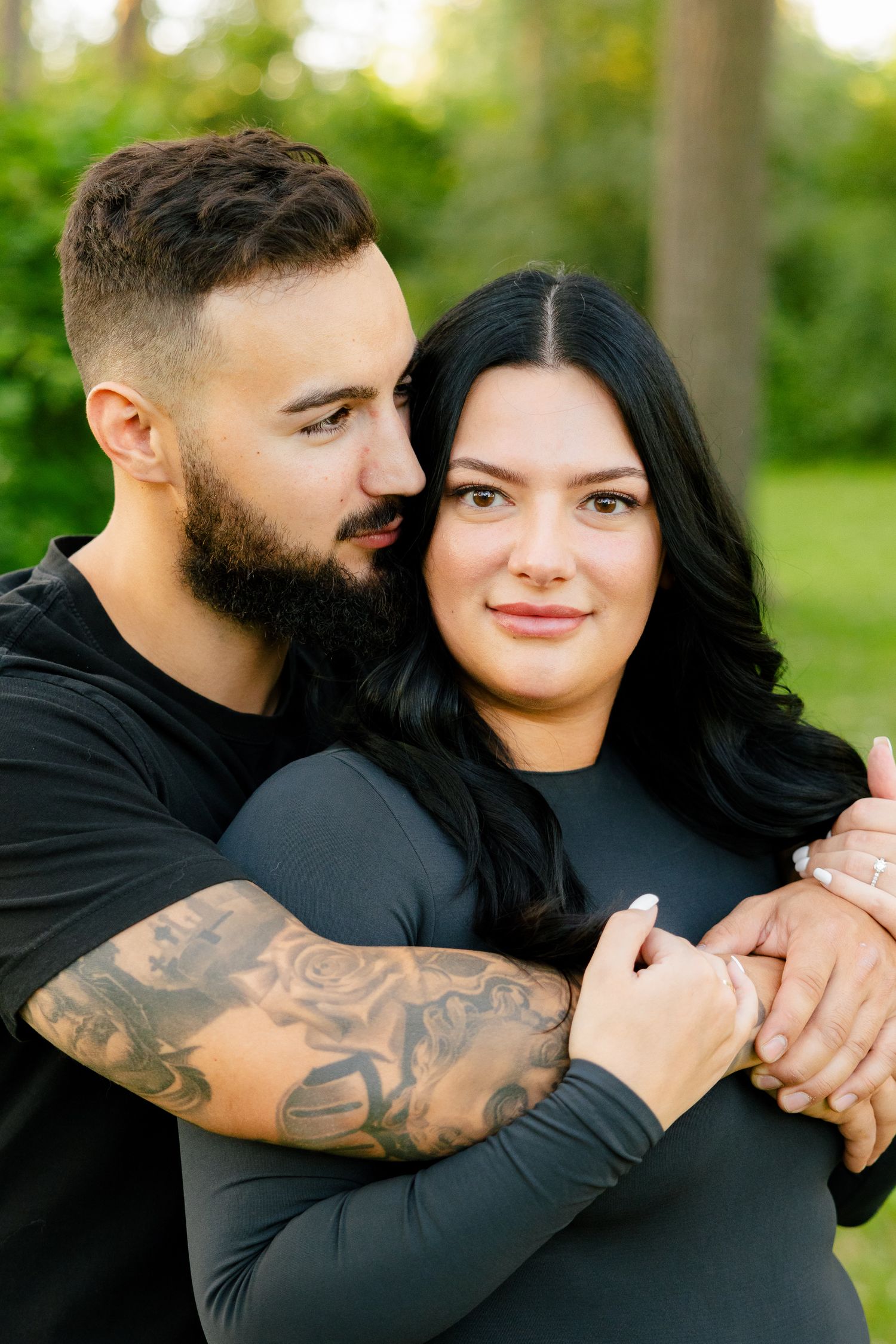 Close-up portrait of couple sharing tender moment in park with green foliage background.