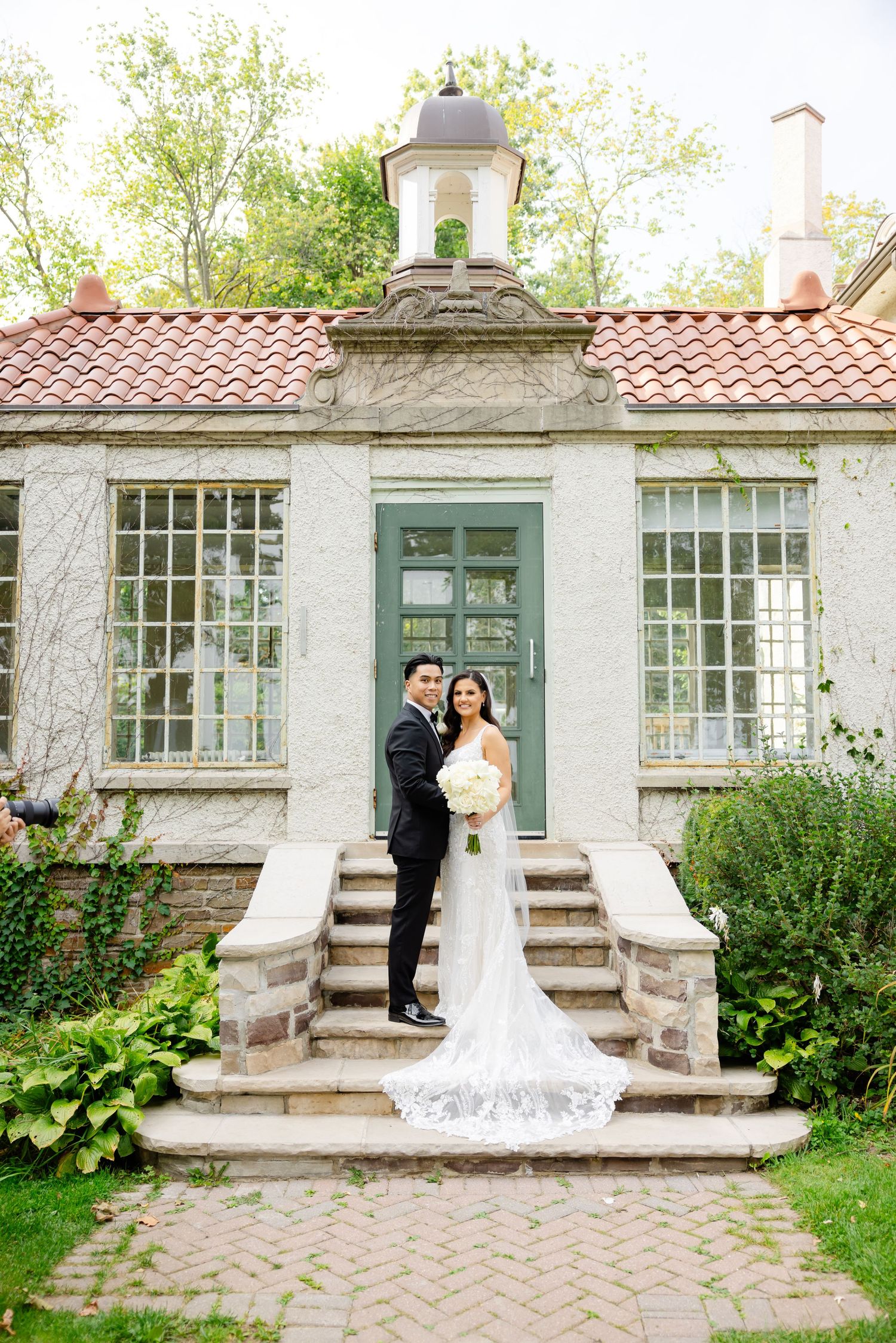 Newlyweds pose on stone steps of a charming historic building with trailing garden vines.