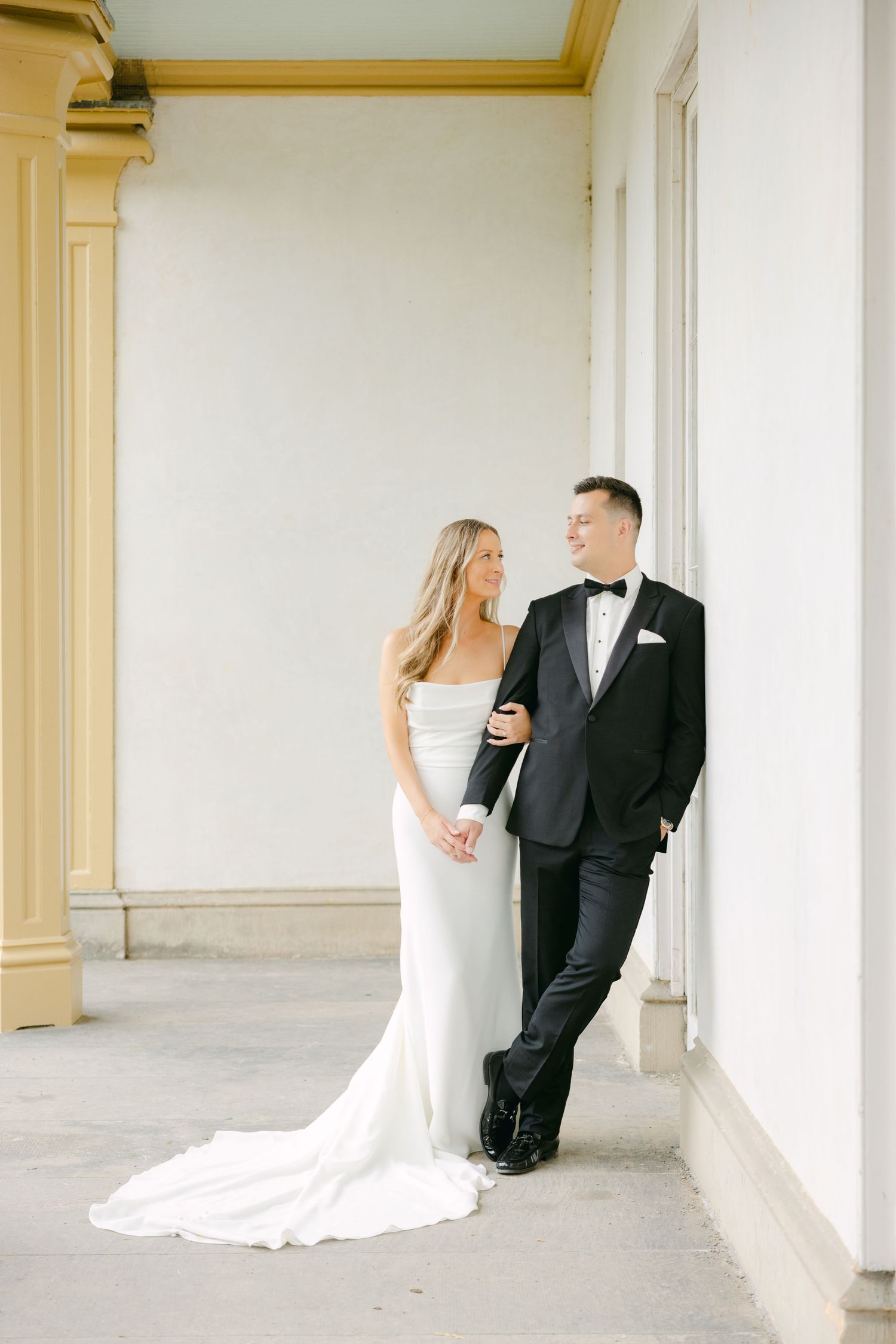 Wedding couple sharing intimate moment against white wall with gold architectural details.