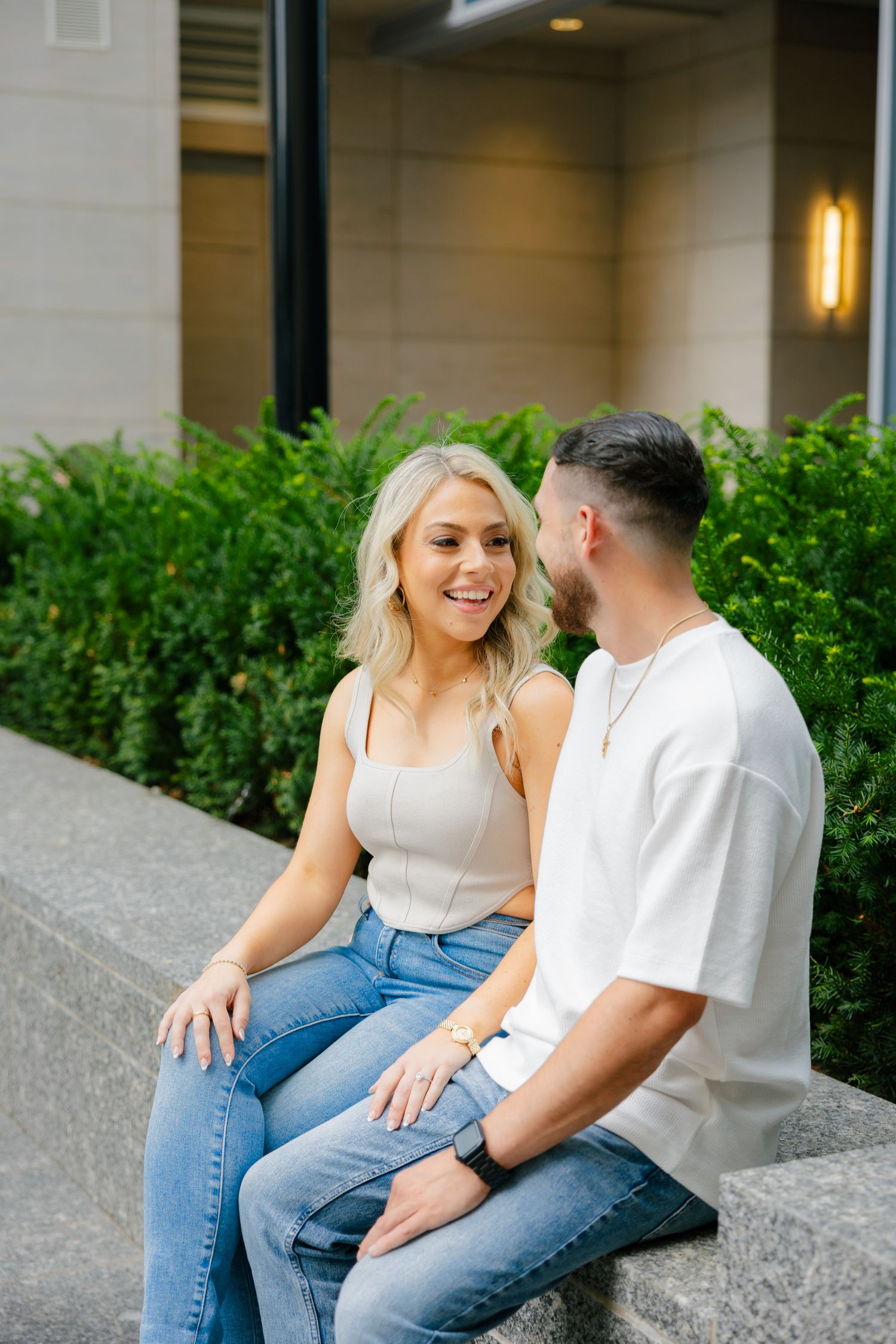 A couple sharing a happy moment while sitting on concrete steps near landscaped bushes.
