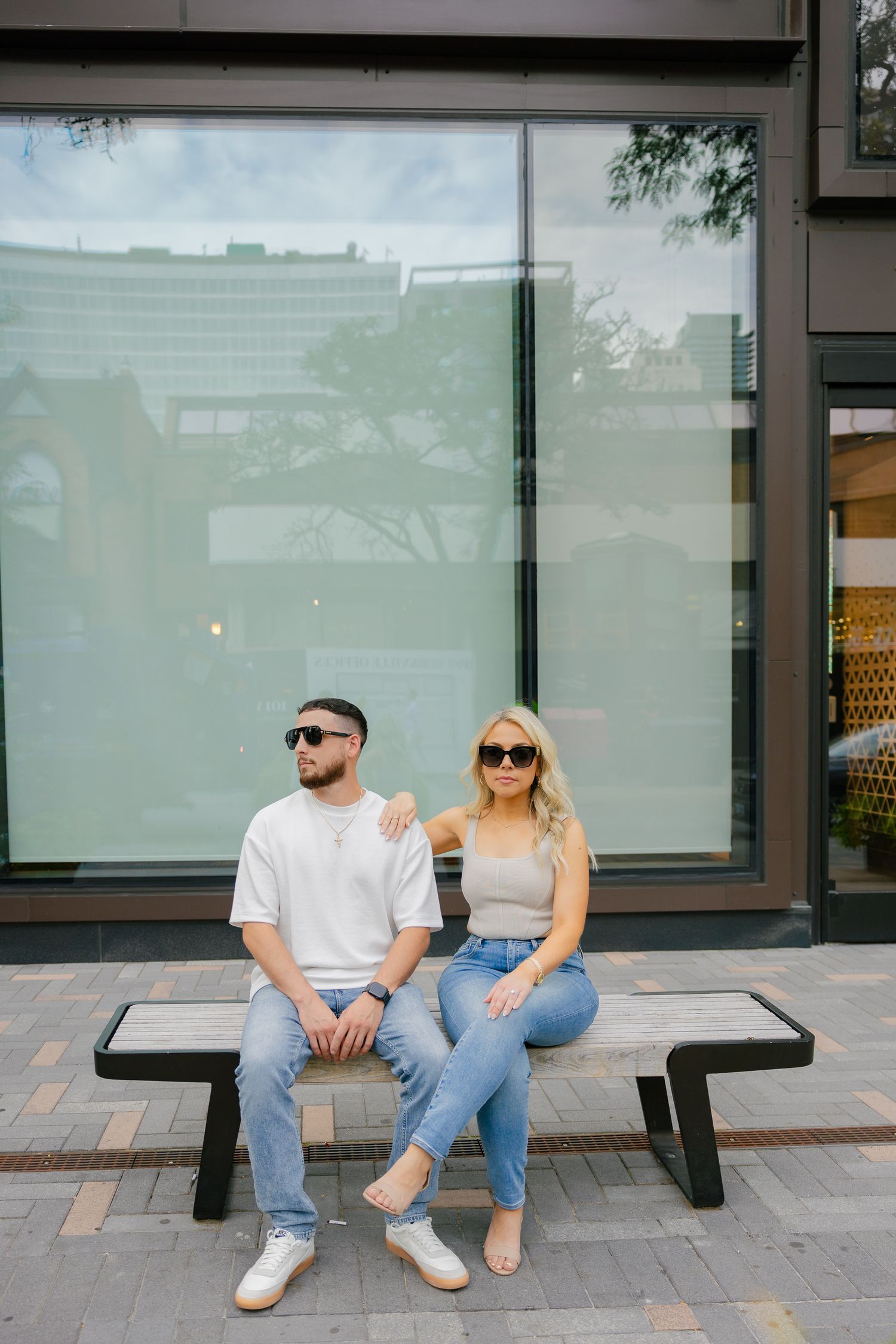 Trendy couple relaxing on bench outside luxury retail store.