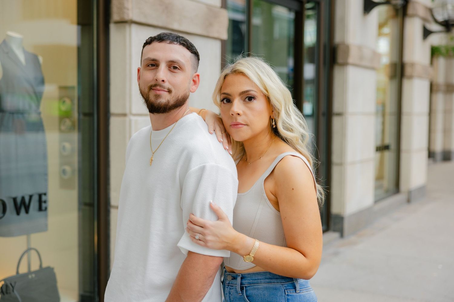 Romantic couple in casual attire standing close together outside storefront.