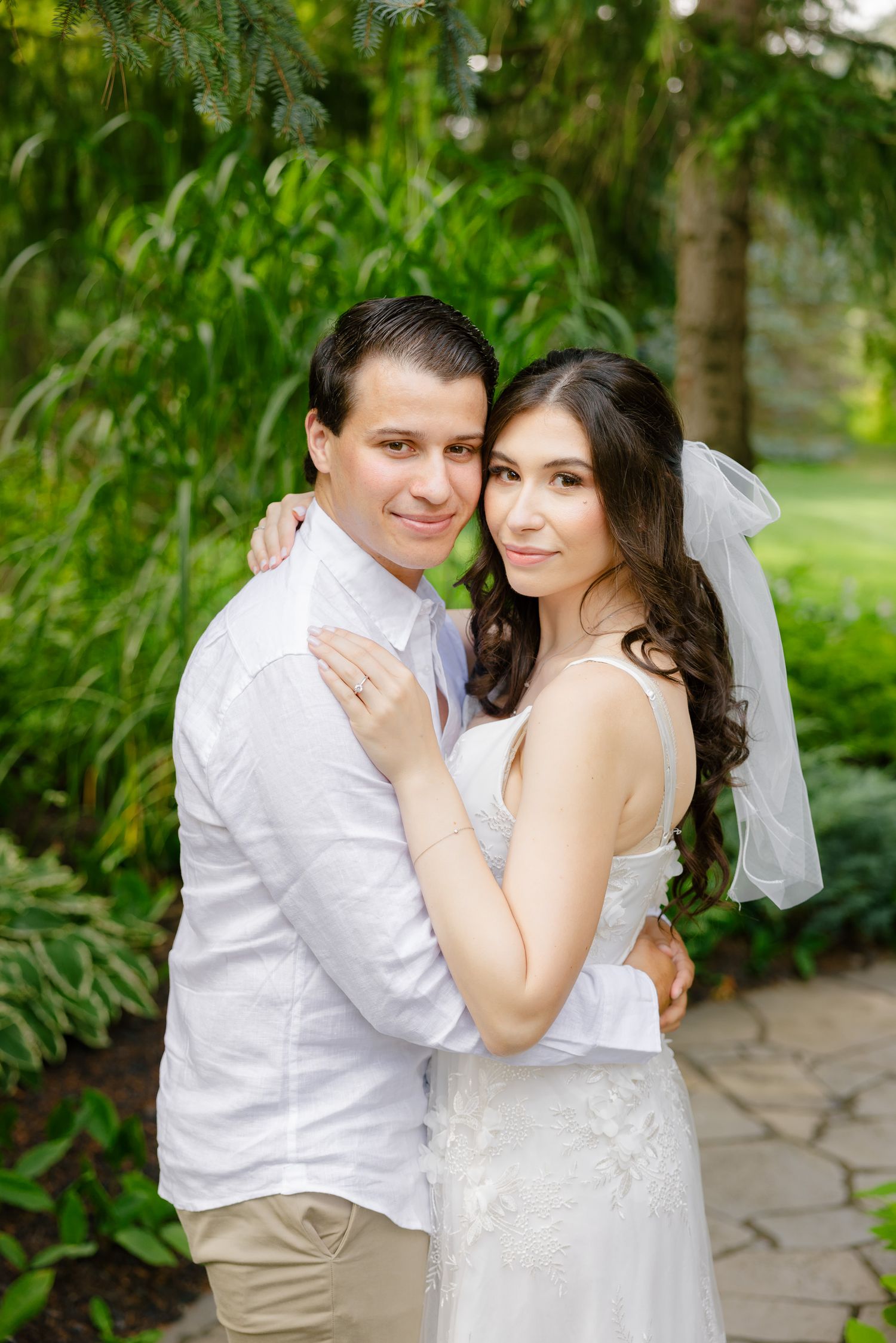Happy couple poses together in garden setting wearing white wedding attire.
