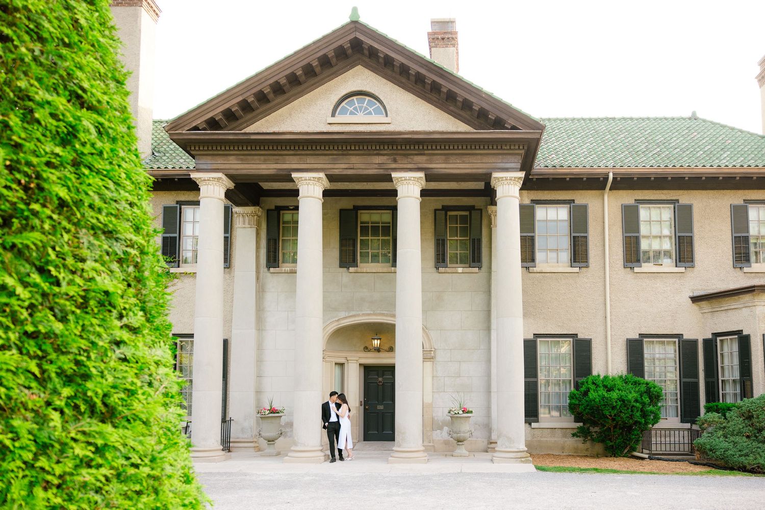 Distant view of couple in formal wear standing at entrance of historic mansion with columns.