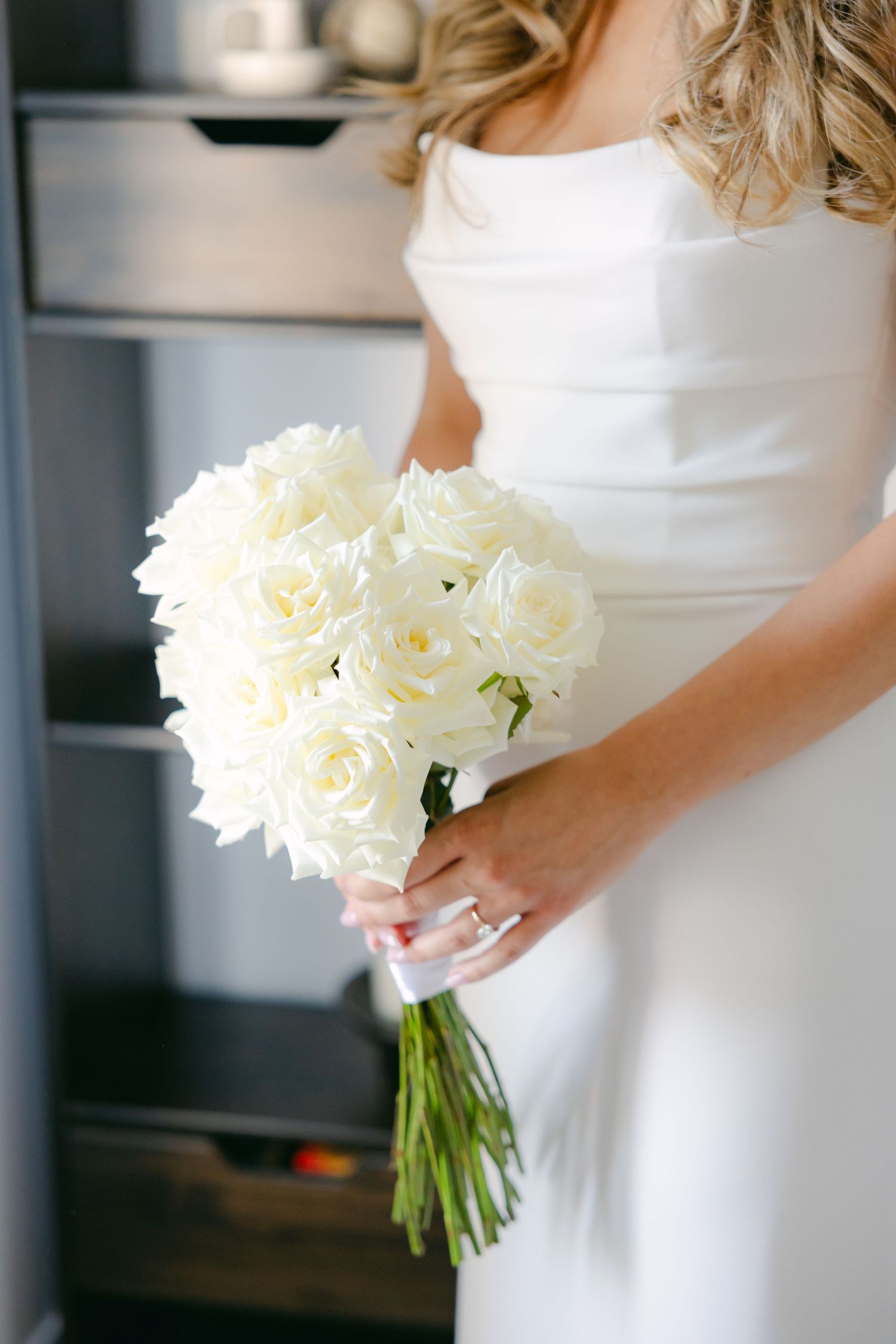Close-up of white bridal bouquet held against elegant wedding dress.