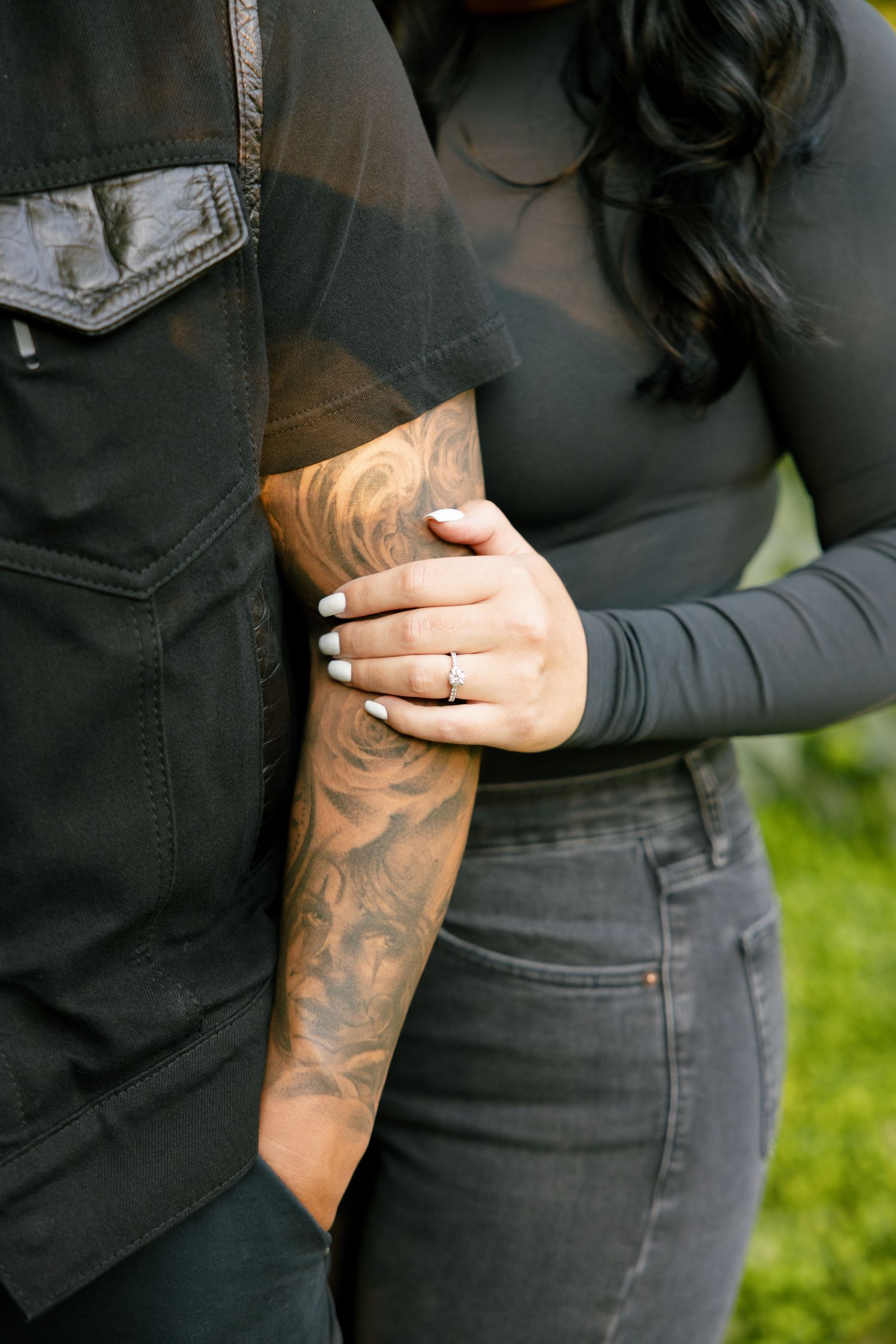 Close-up of a ring and tattooed arm with hands embracing in casual attire.