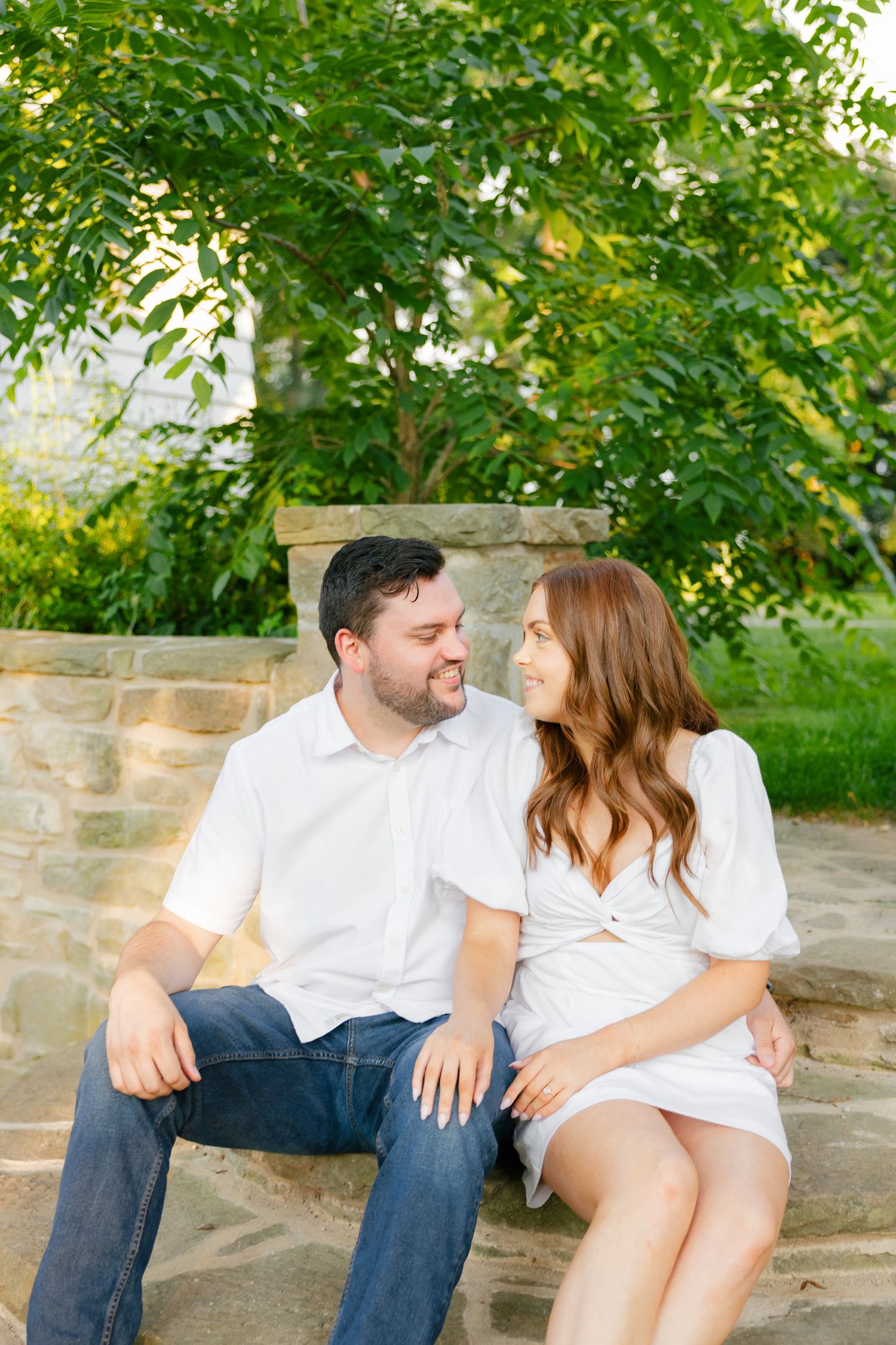 Casual outdoor portrait of couple in white clothing sitting together on stone steps.