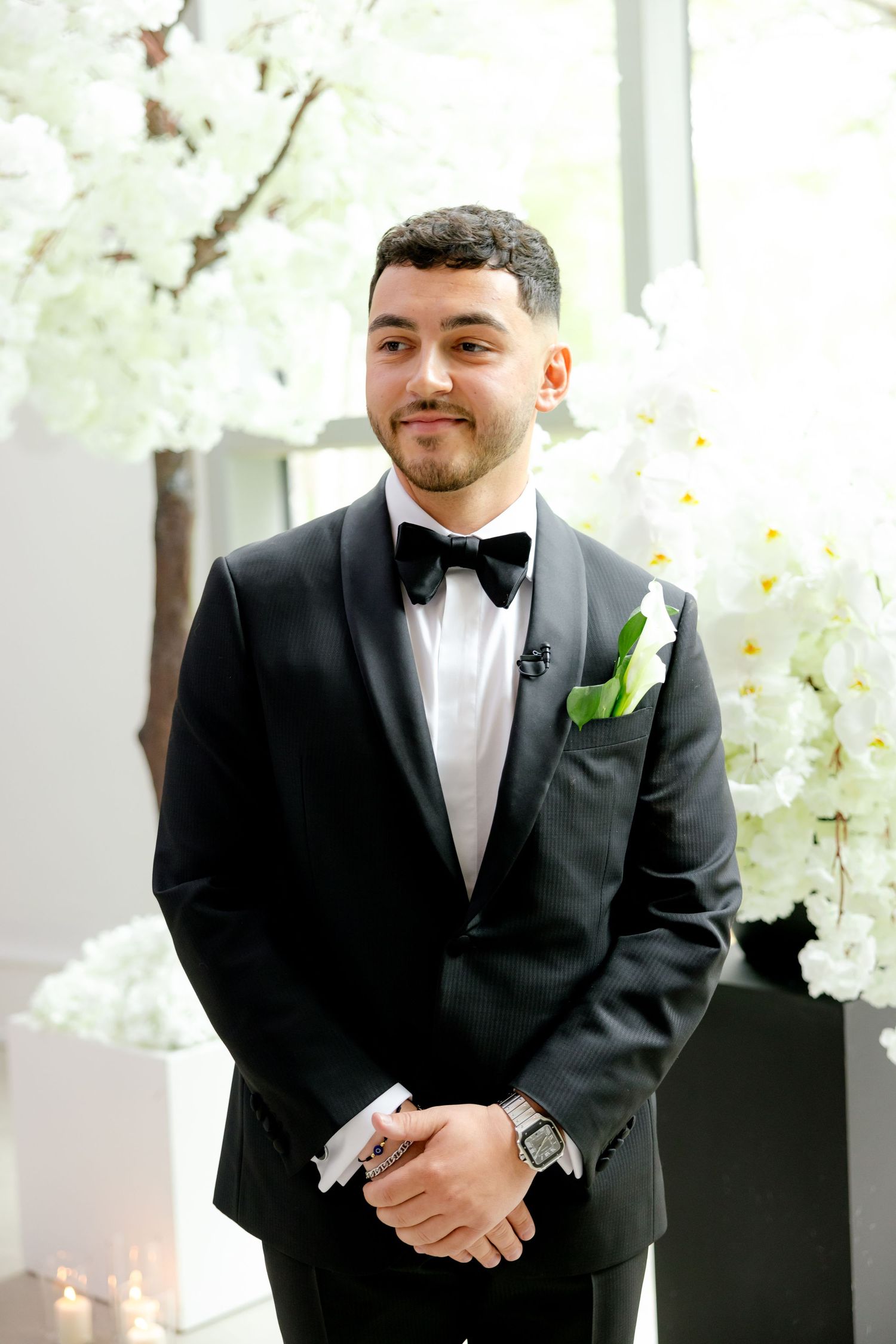 Wedding attire with black tuxedo and green boutonniere in bright venue setting.