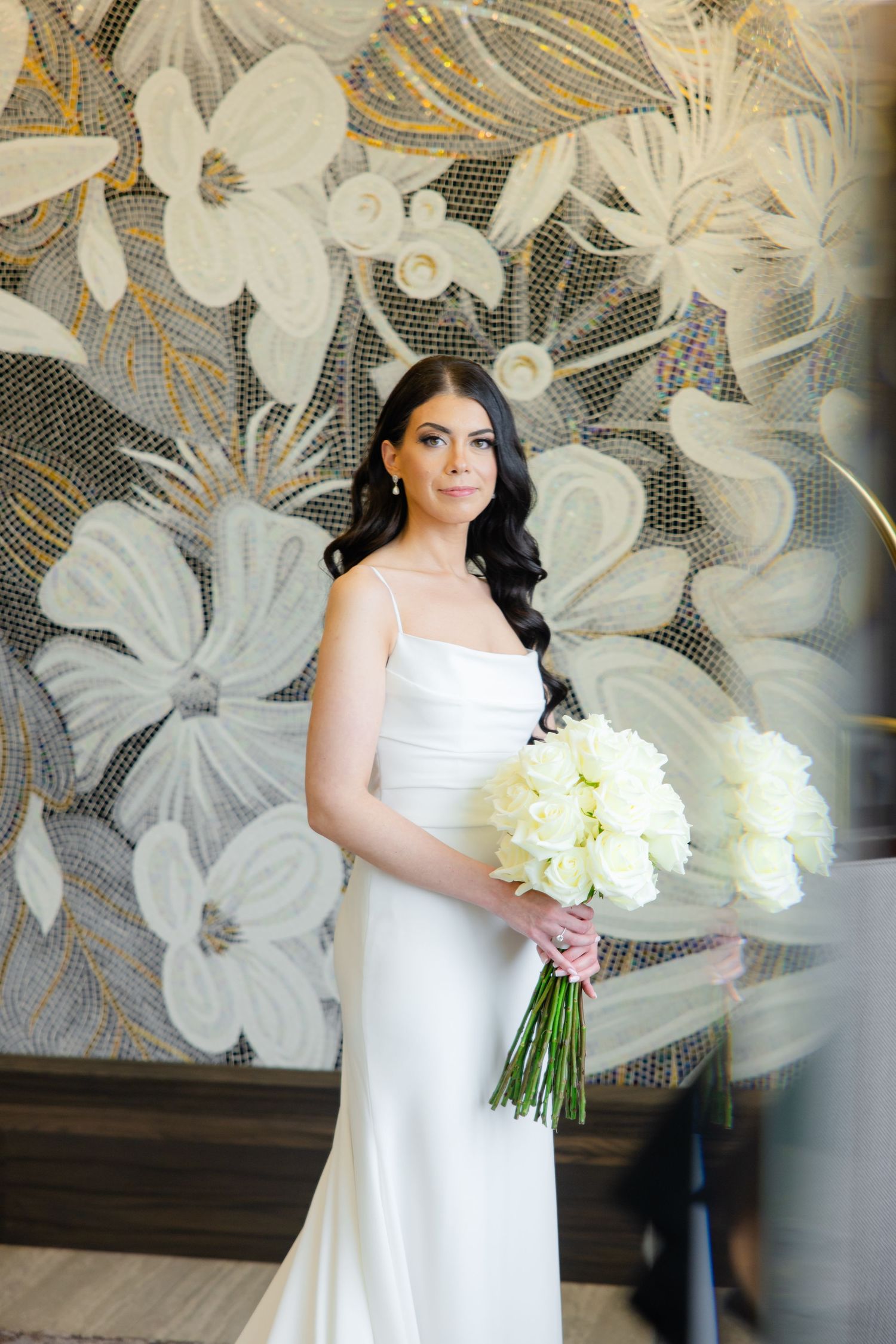Elegant bridal portrait with white flowers against a decorative gray and gold floral wall backdrop.