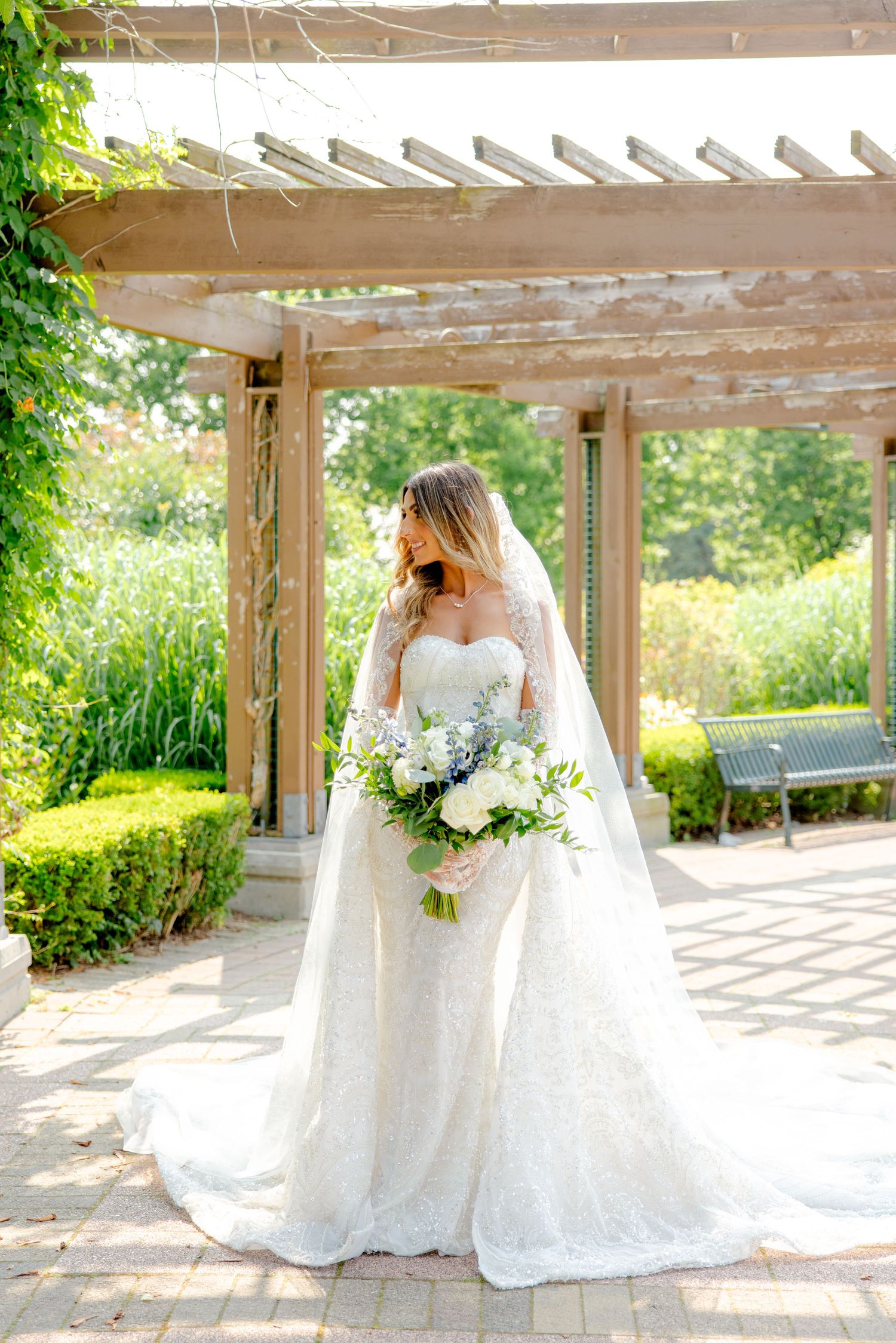 Side-angle bridal portrait showcasing detailed lace dress and cascading floral bouquet in garden setting.