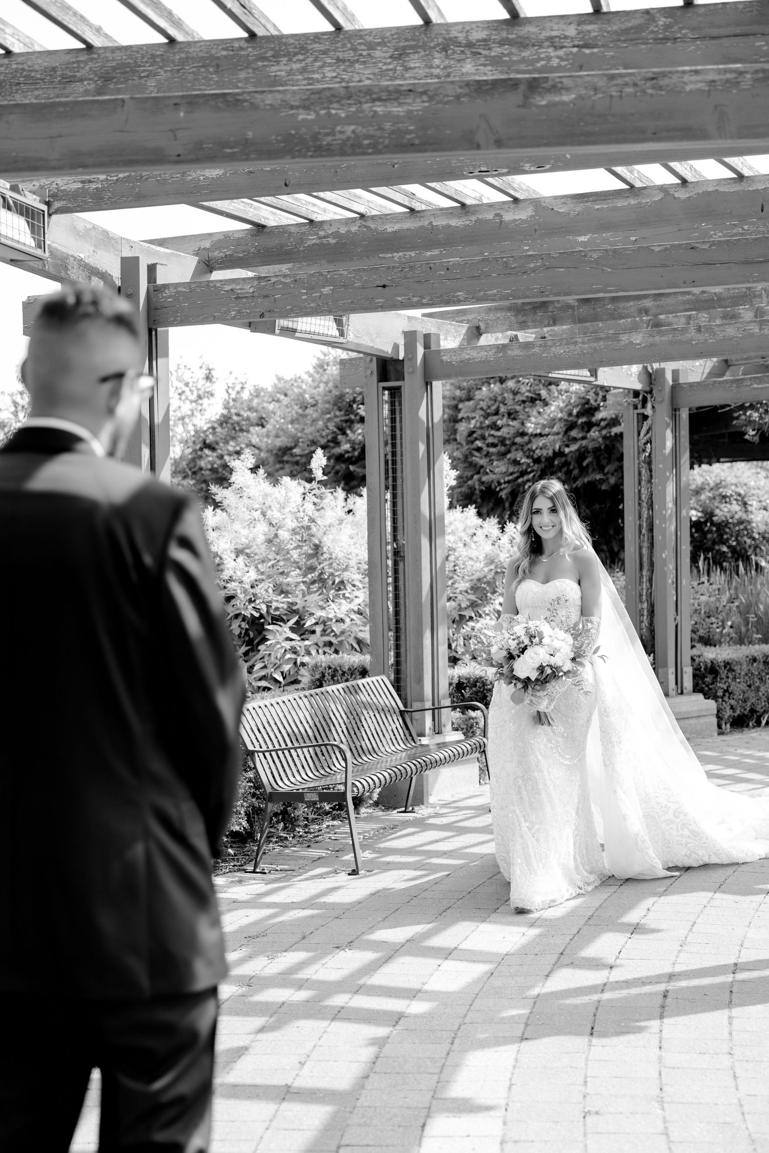 Black and white first look moment between couple under rustic pergola.