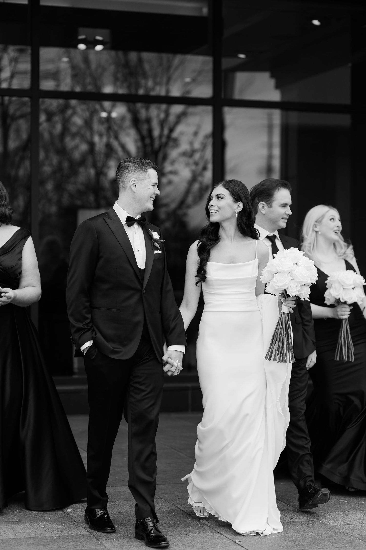 Black and white photo of wedding party walking and laughing together outside.