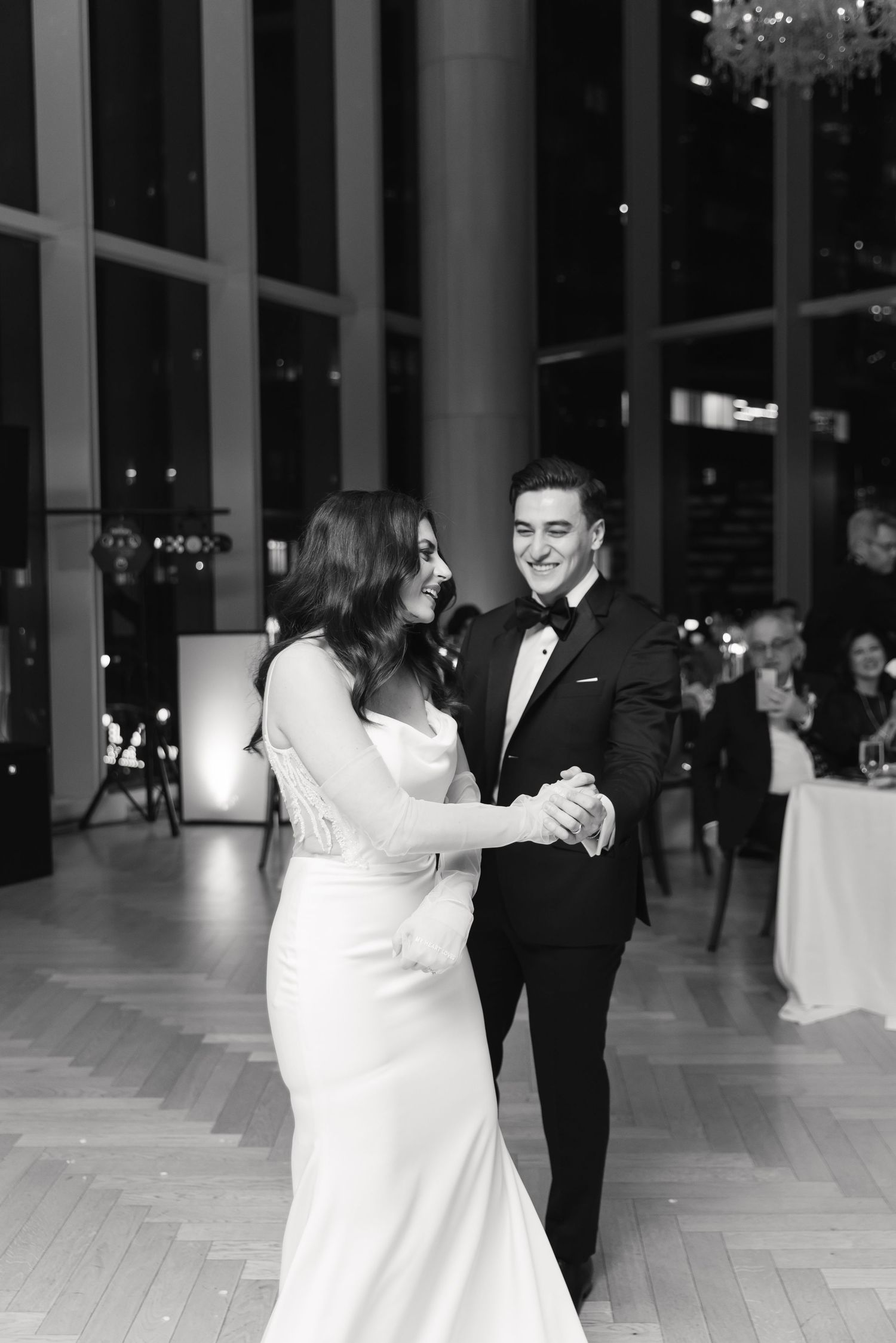 A romantic first dance between newlyweds in a elegant venue with floor-to-ceiling windows.
