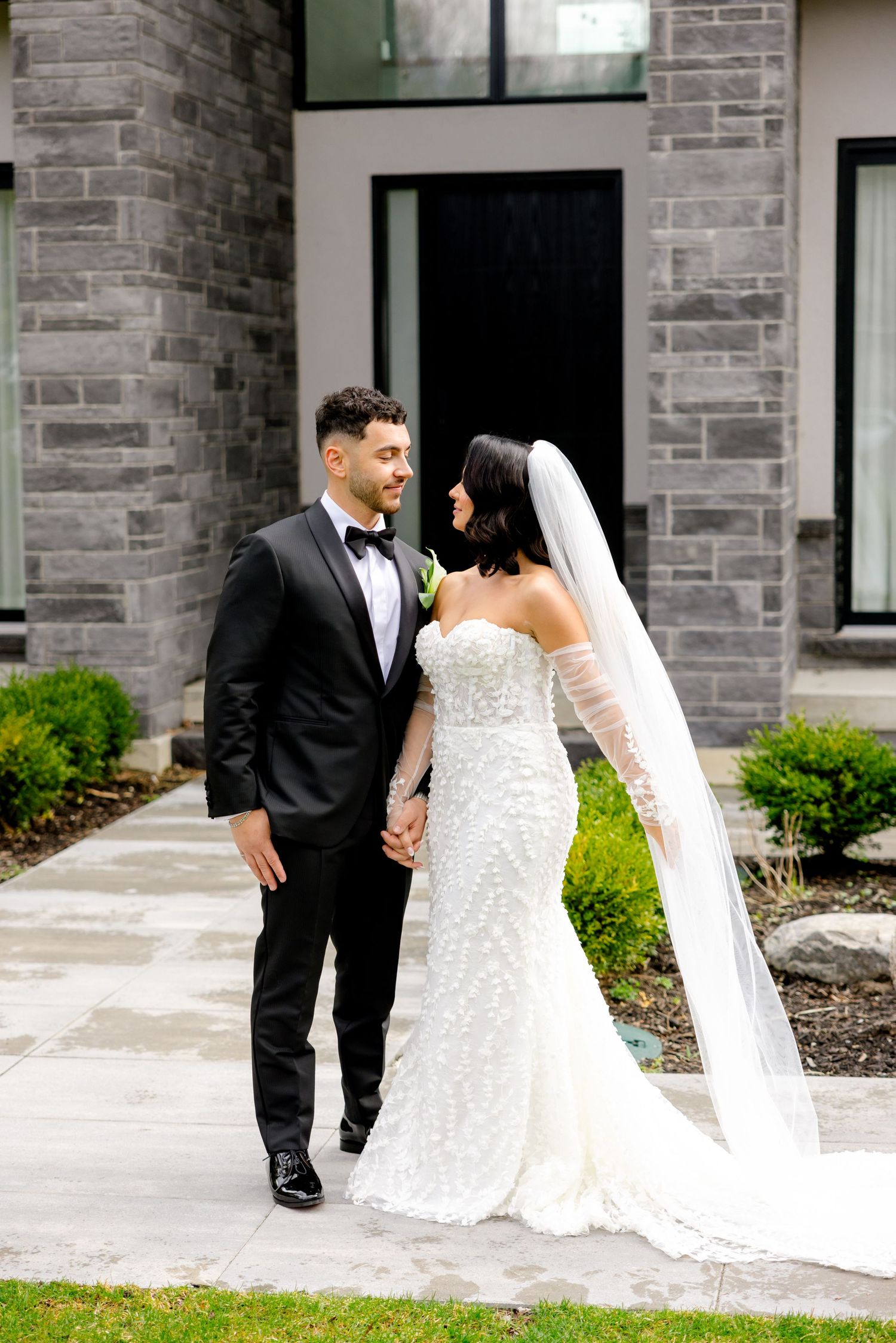 A romantic wedding portrait of a couple walking together against a modern stone facade.
