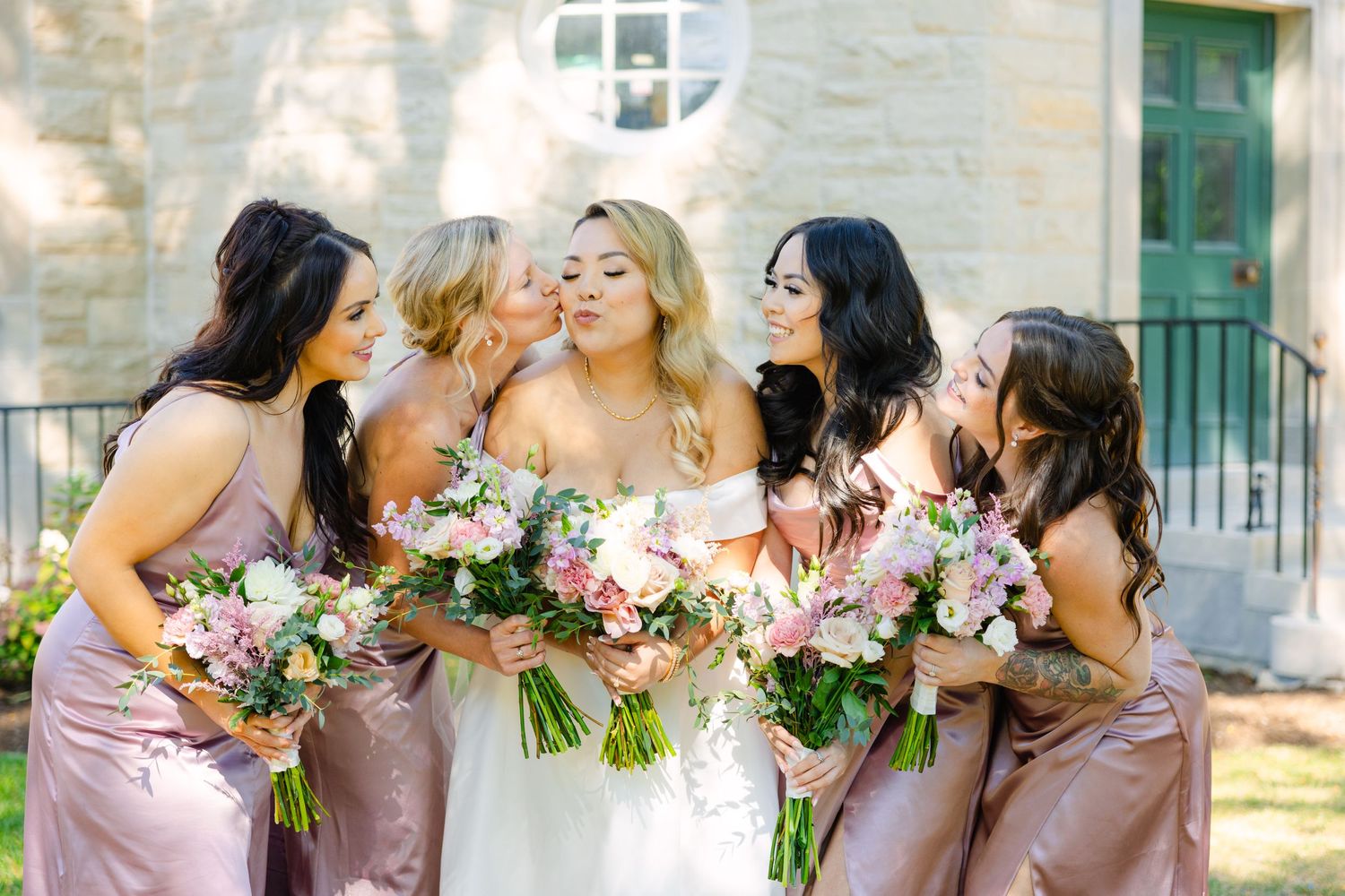 Candid moment of bridal party laughing together while holding pink and white bouquets.