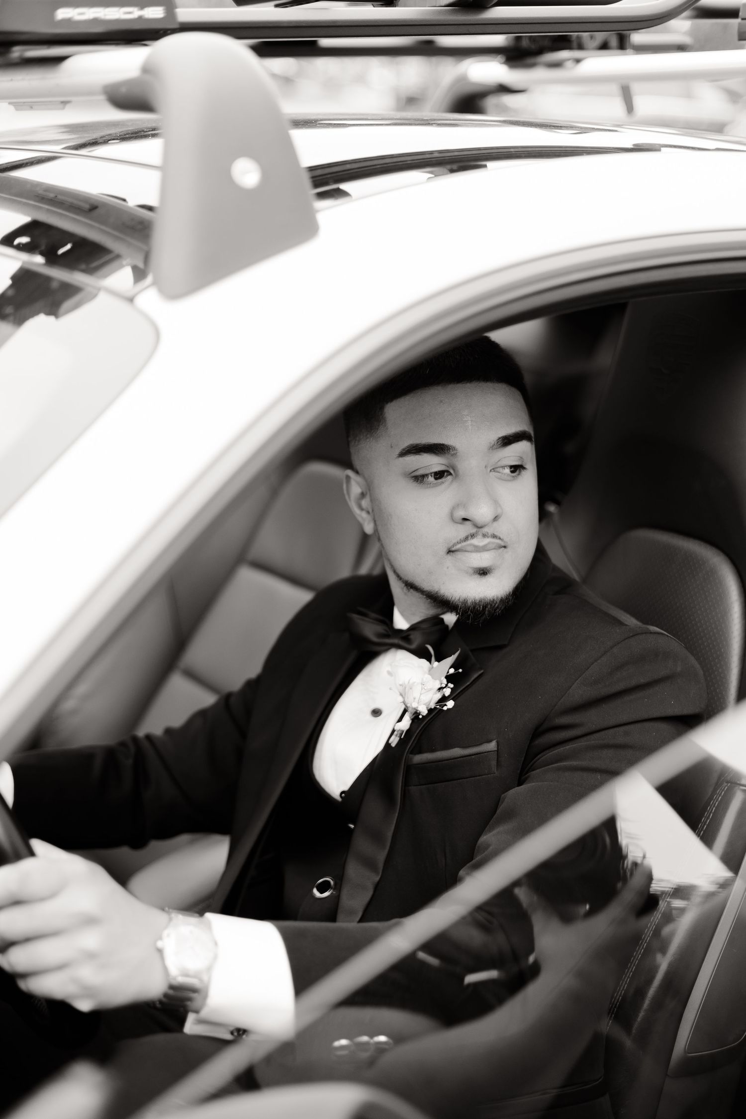 Black and white portrait of person in tuxedo seated in driver's seat.