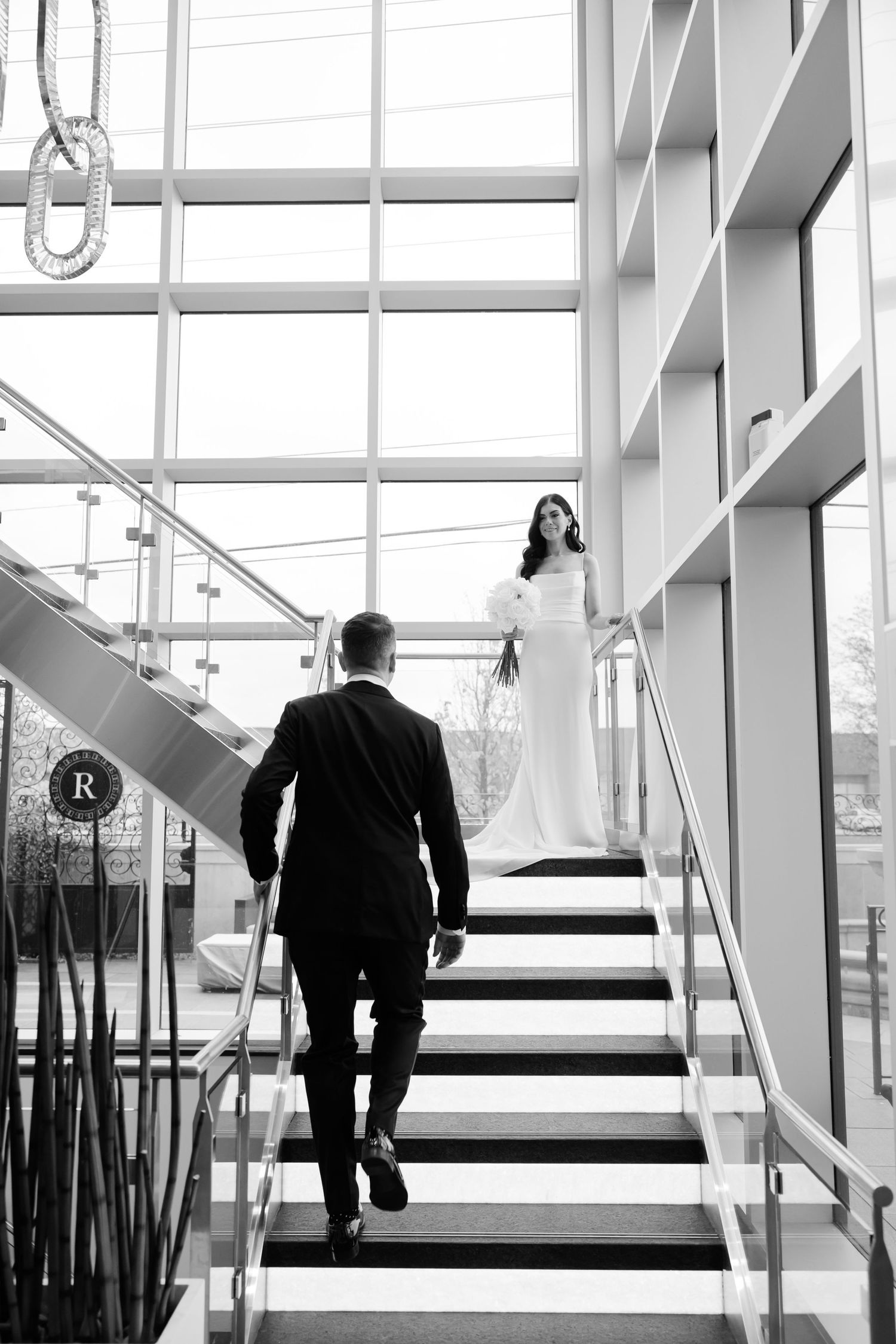 Black and white photo of couple on modern staircase with geometric window patterns.