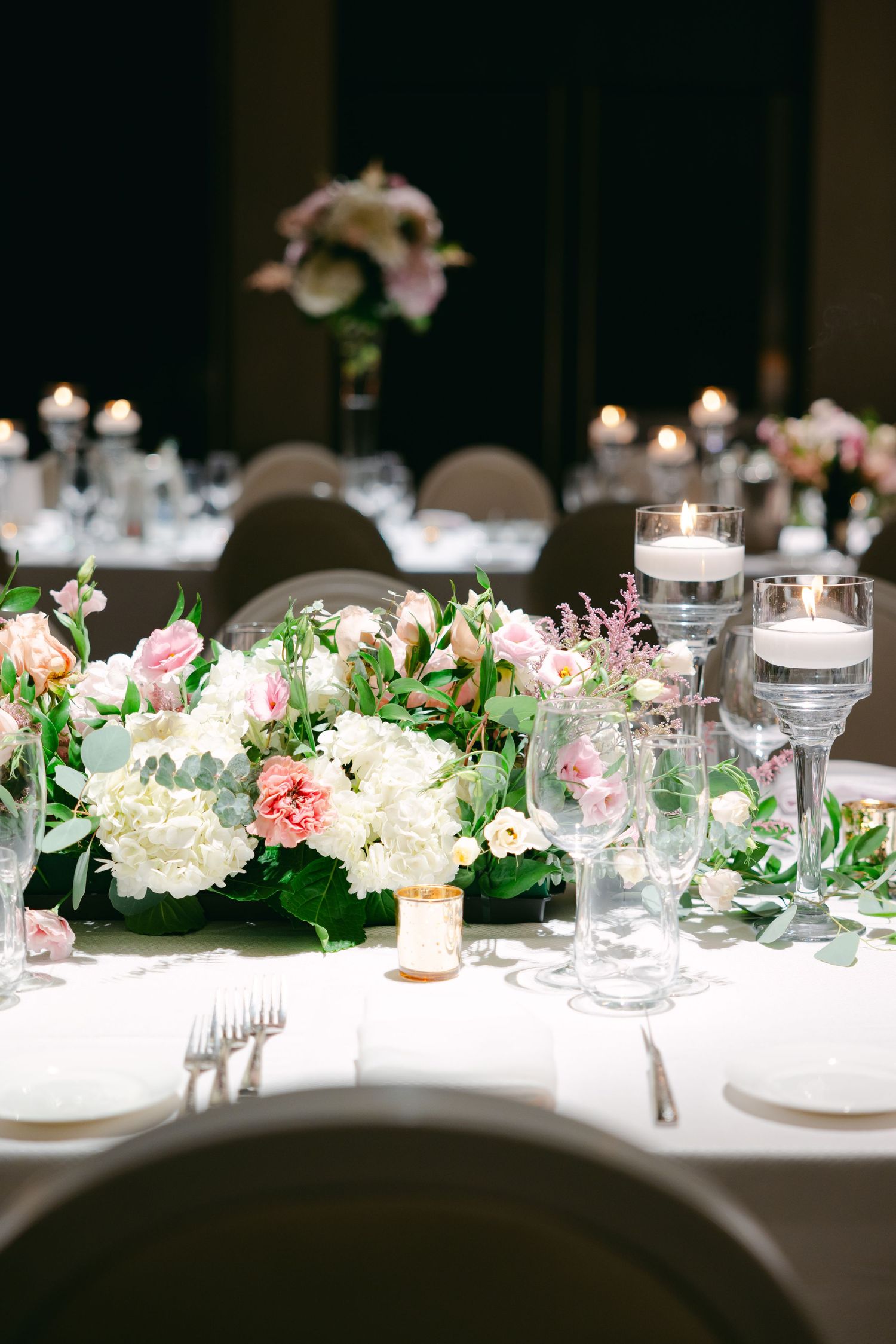 Elegant reception table with hydrangeas, roses, and floating candles in glass vessels.