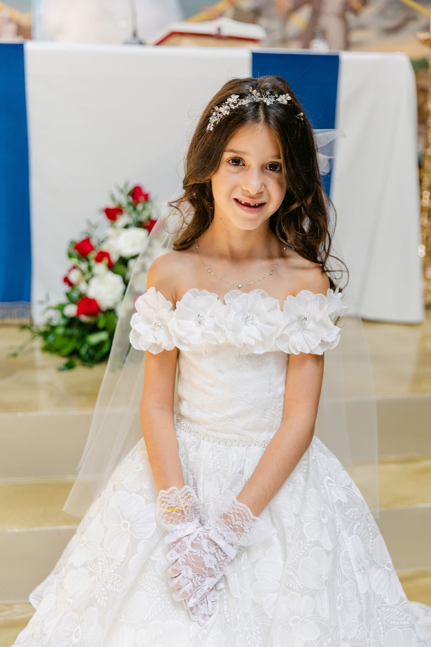 Young participant in a white ceremonial dress standing in an ornate church setting.