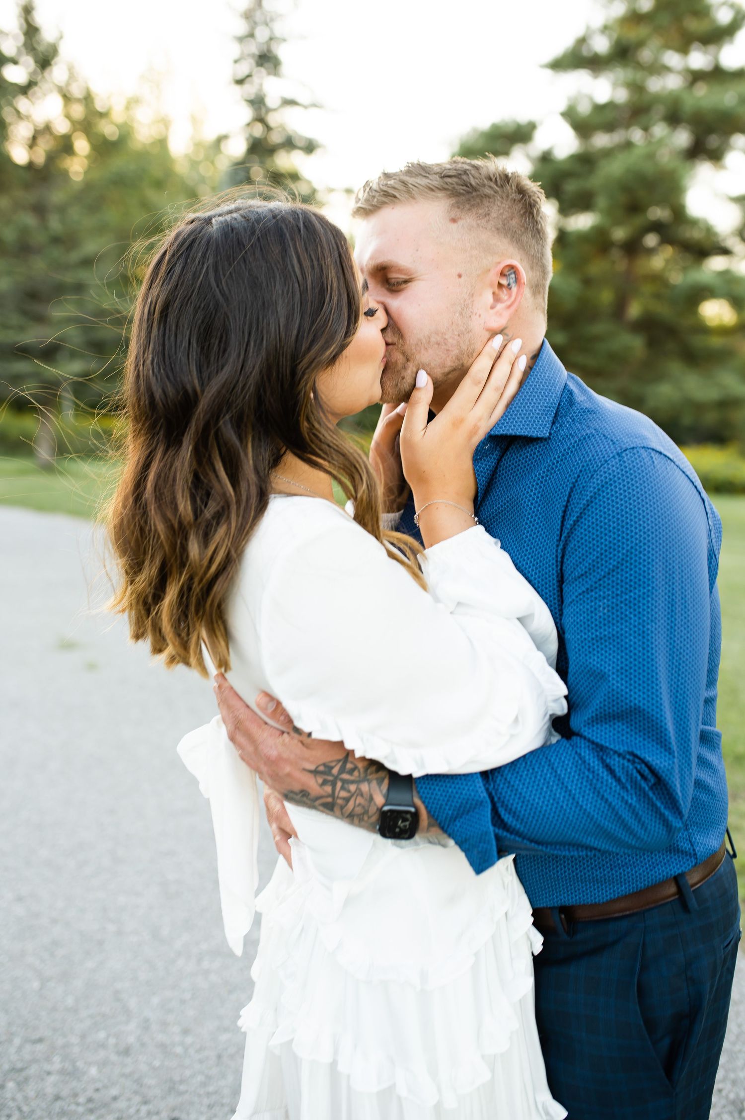 Romantic couple embracing in tender moment on outdoor path with evergreen trees.