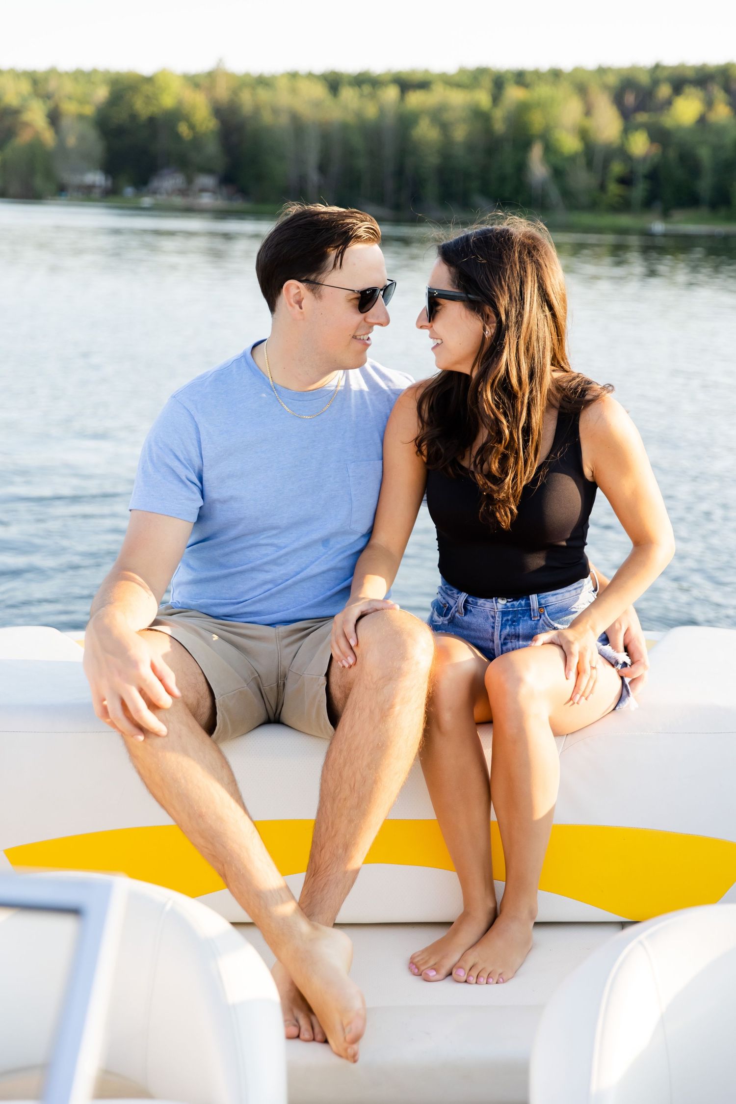 Couple sitting on yellow and white boat deck wearing sunglasses and casual summer attire.